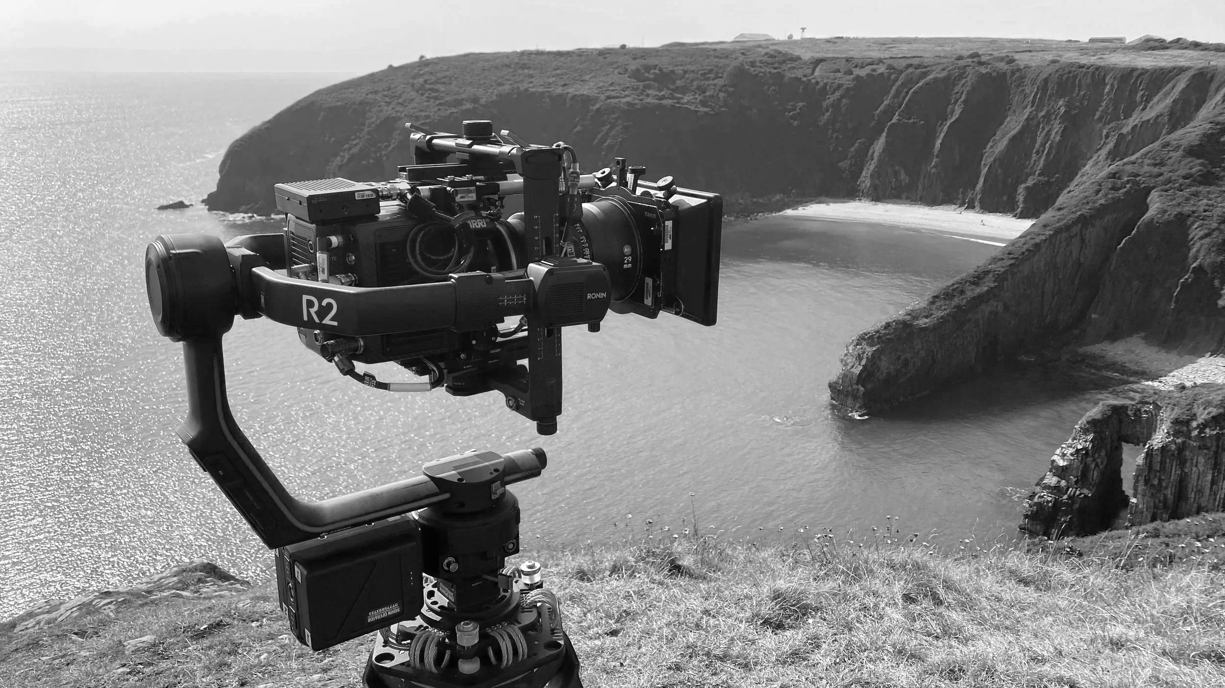 Camera on a tripod overlooking a coastal landscape with cliffs and the ocean, black and white photo.