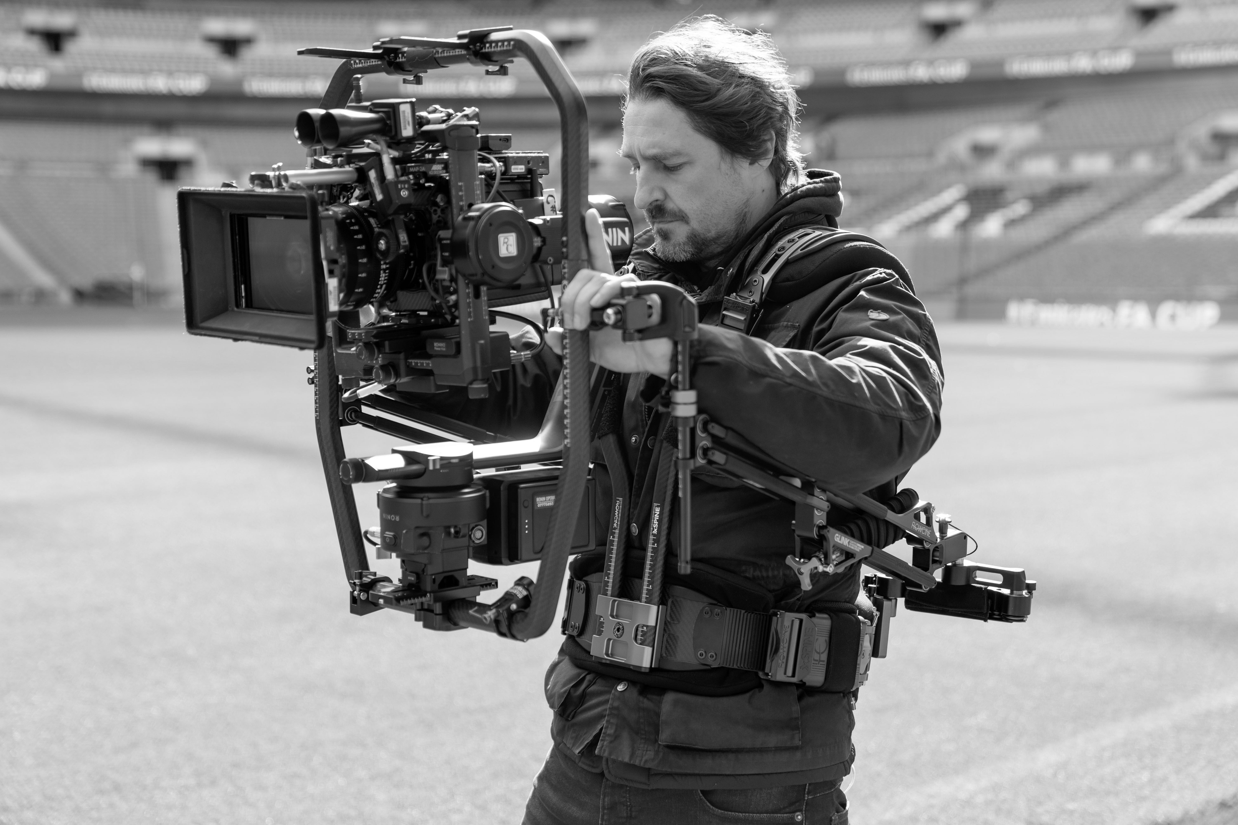 A man operating a professional film camera on a track in an empty stadium.