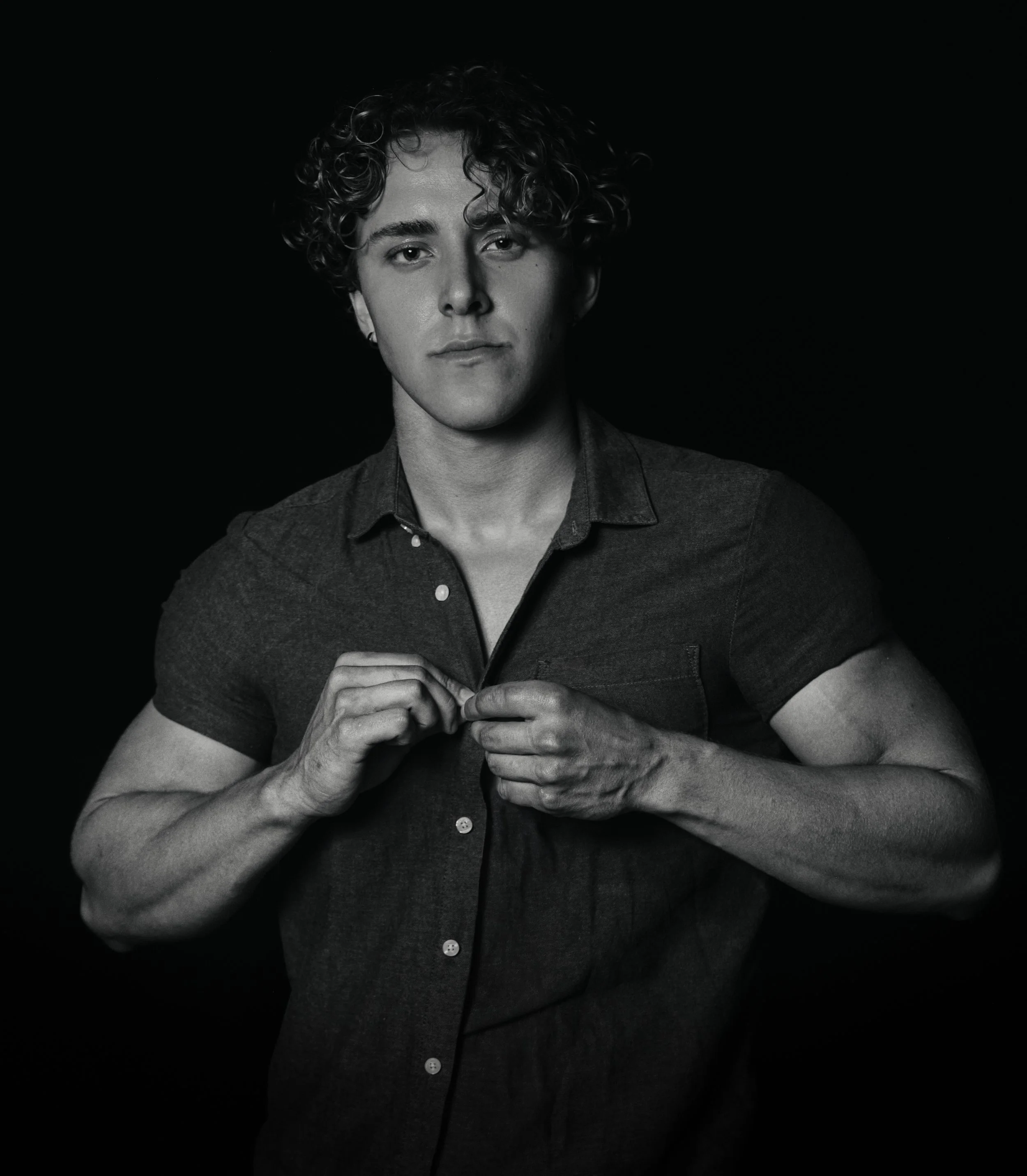 Black and white portrait of a young man with curly hair, looking directly at the camera, wearing a button-up shirt.