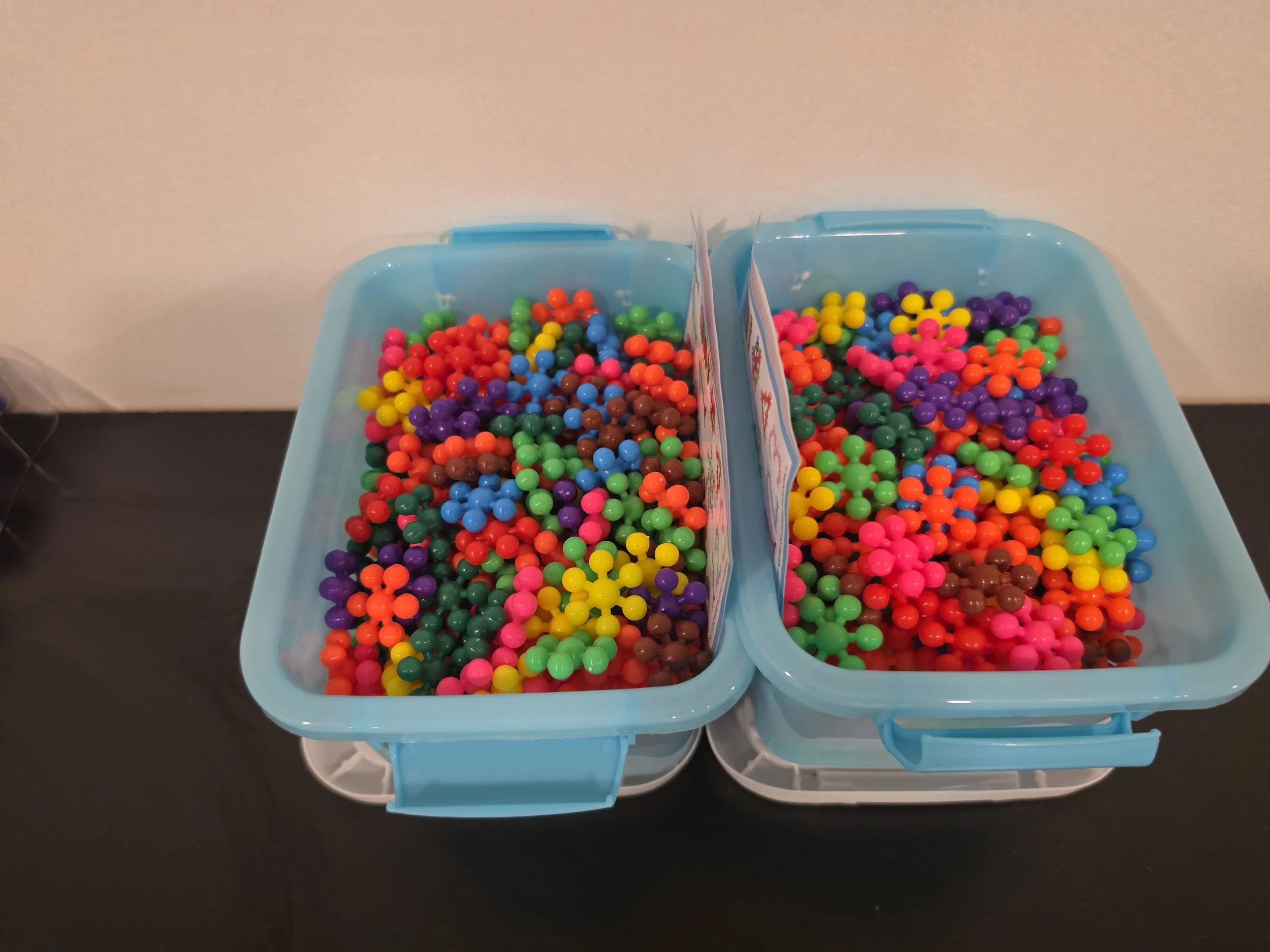 Two blue plastic containers filled with colorful small round beads, separated by a divider.