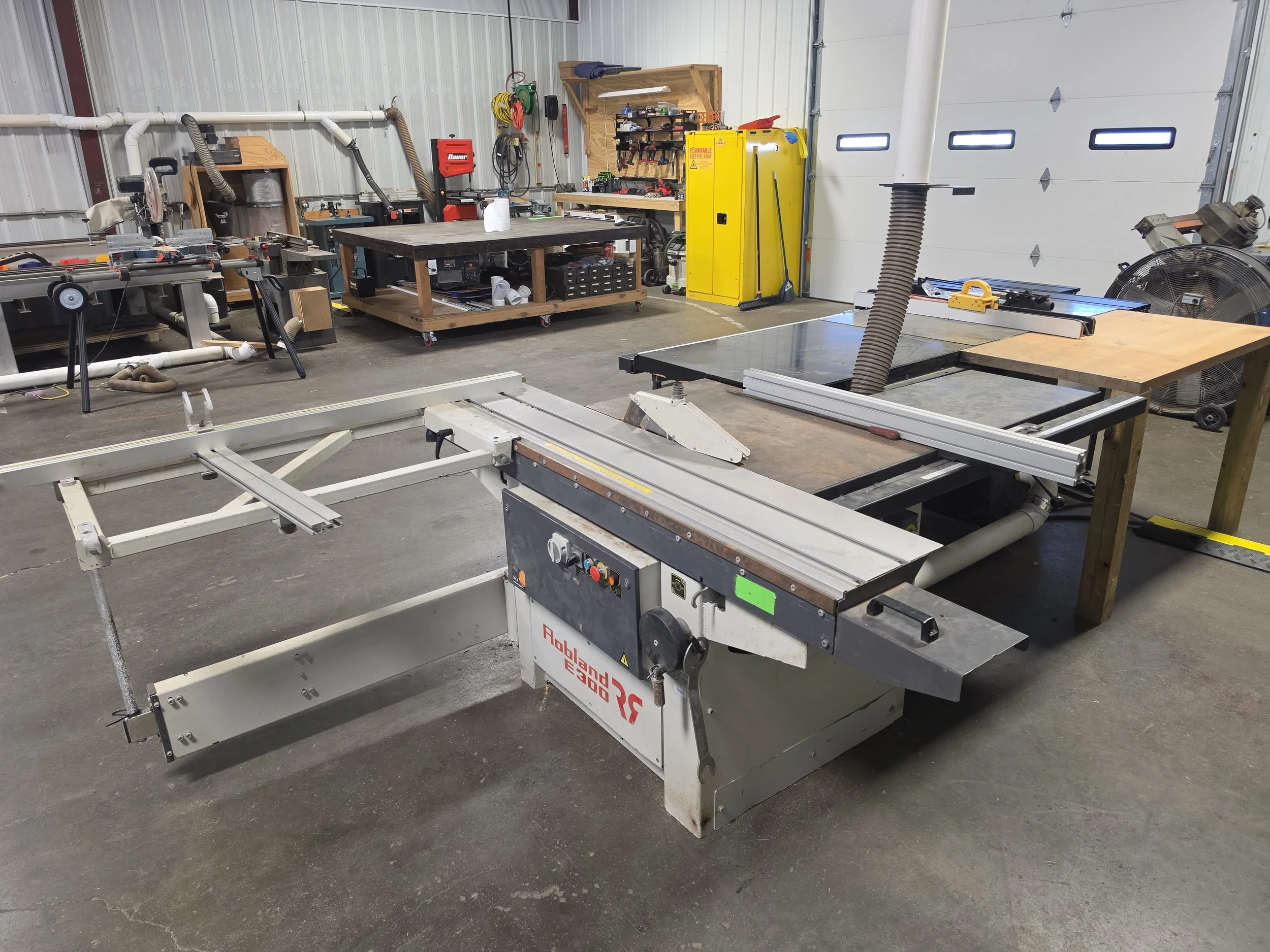 A spacious workshop with tools, workbenches, and woodworking equipment including a large table saw and a dust collection system.