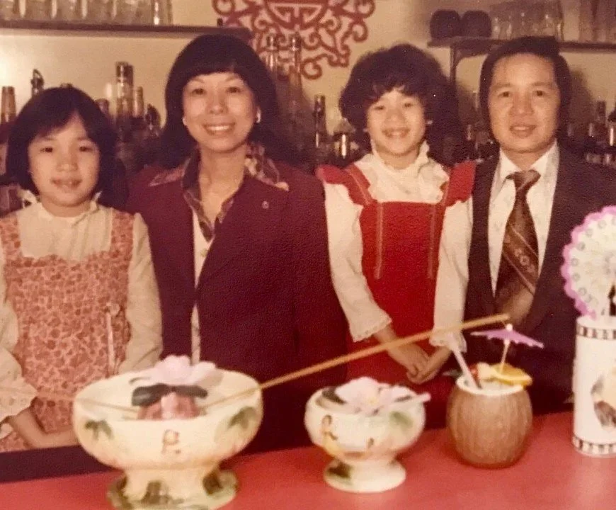 The Wong Family  standing behind a decorated table with bowls, drinks, and a colorful fan, celebrating a special occasion.