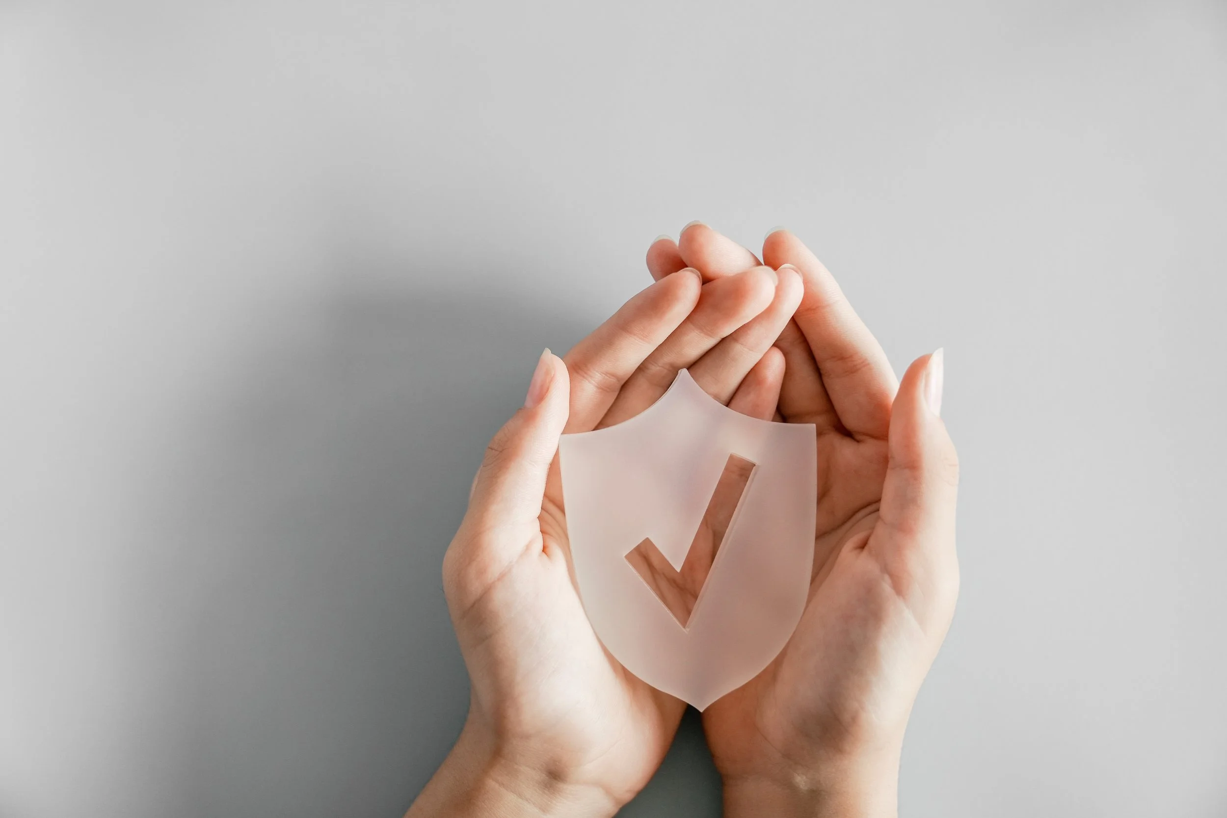 Hands holding a clear plastic ballot with a checkmark sticker, against a plain gray background.