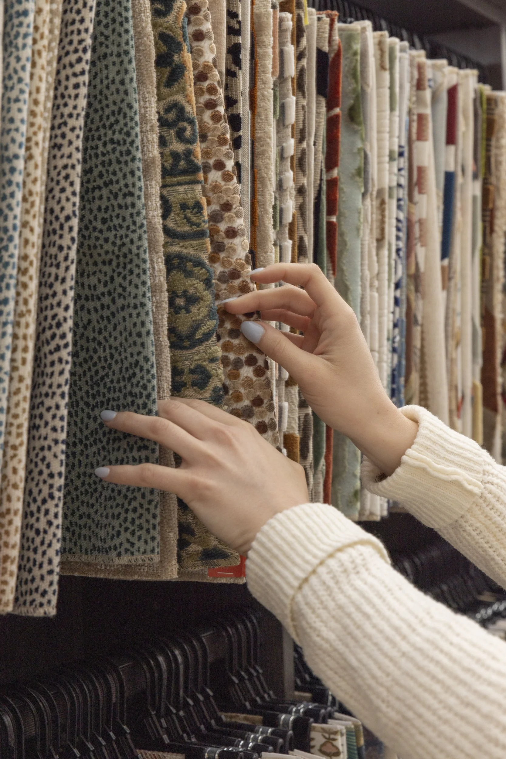 Person shopping for rugs or carpets at a store, holding and examining a rug among other rugs hanging on display.