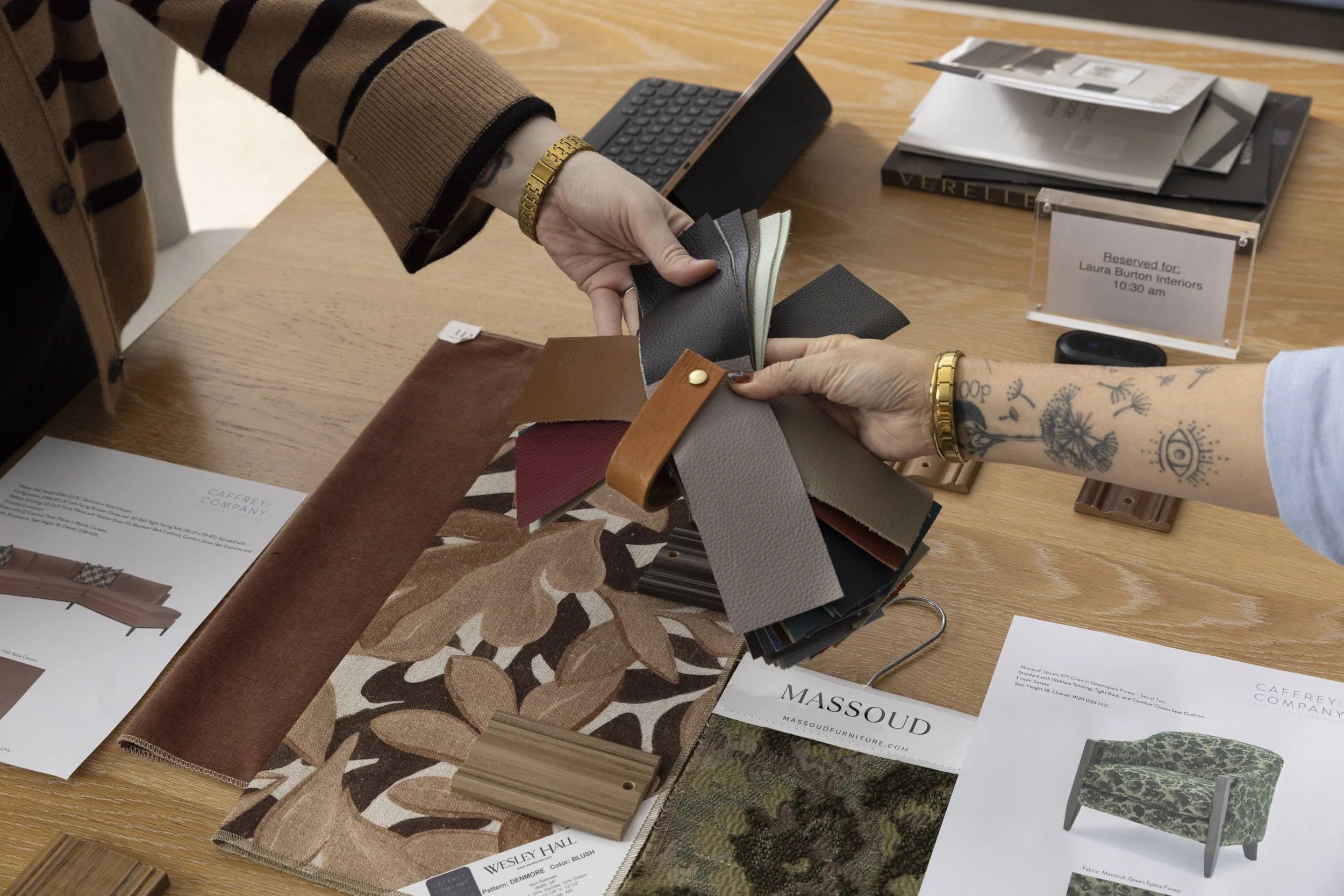 A designer's workspace with fabric and material swatches, a small electronic device, and sample books for interior design.