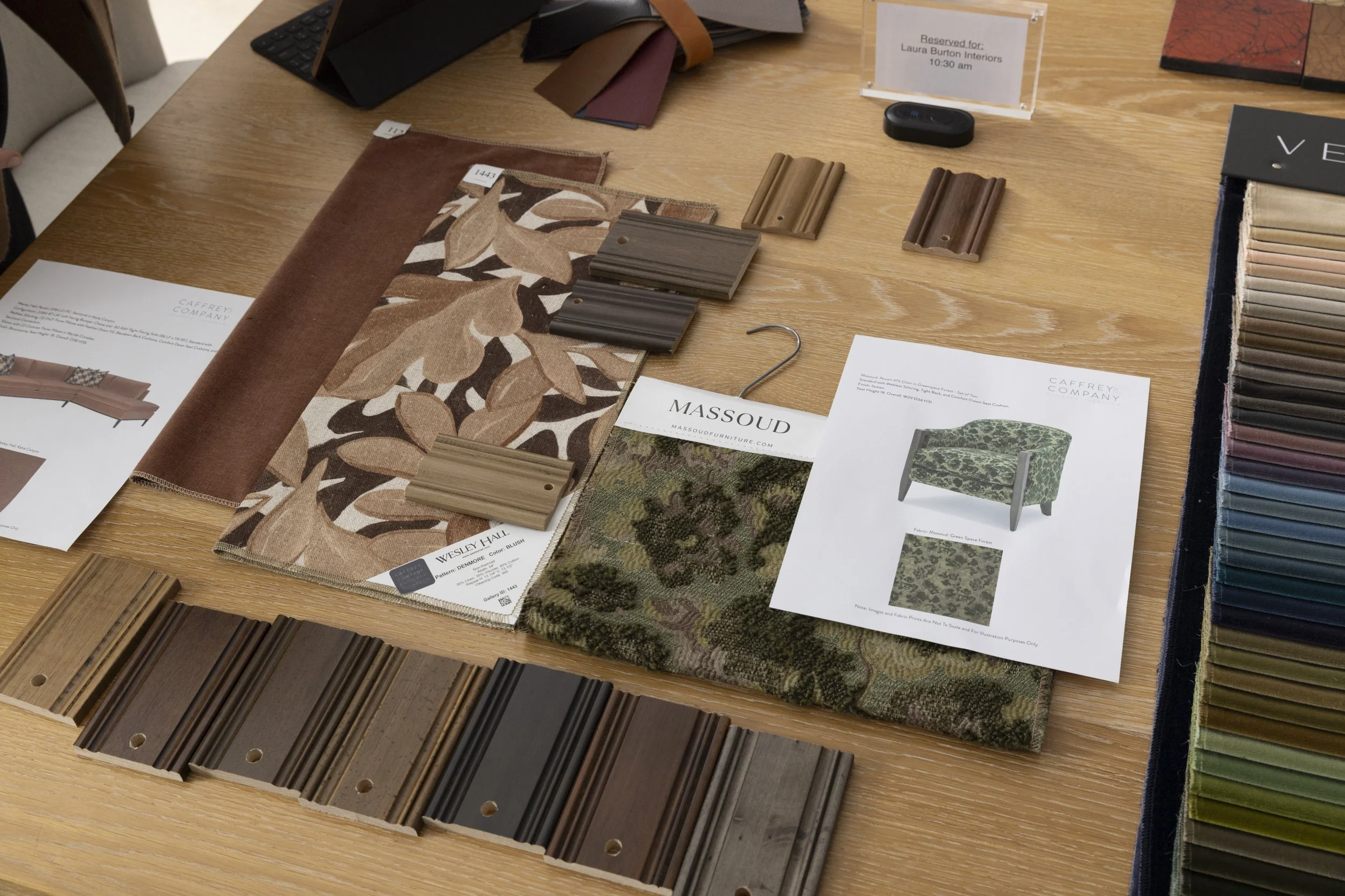 A display of fabric samples, color swatches, and decorative trim pieces on a wooden table, with sample books and informational sheets for interior design.