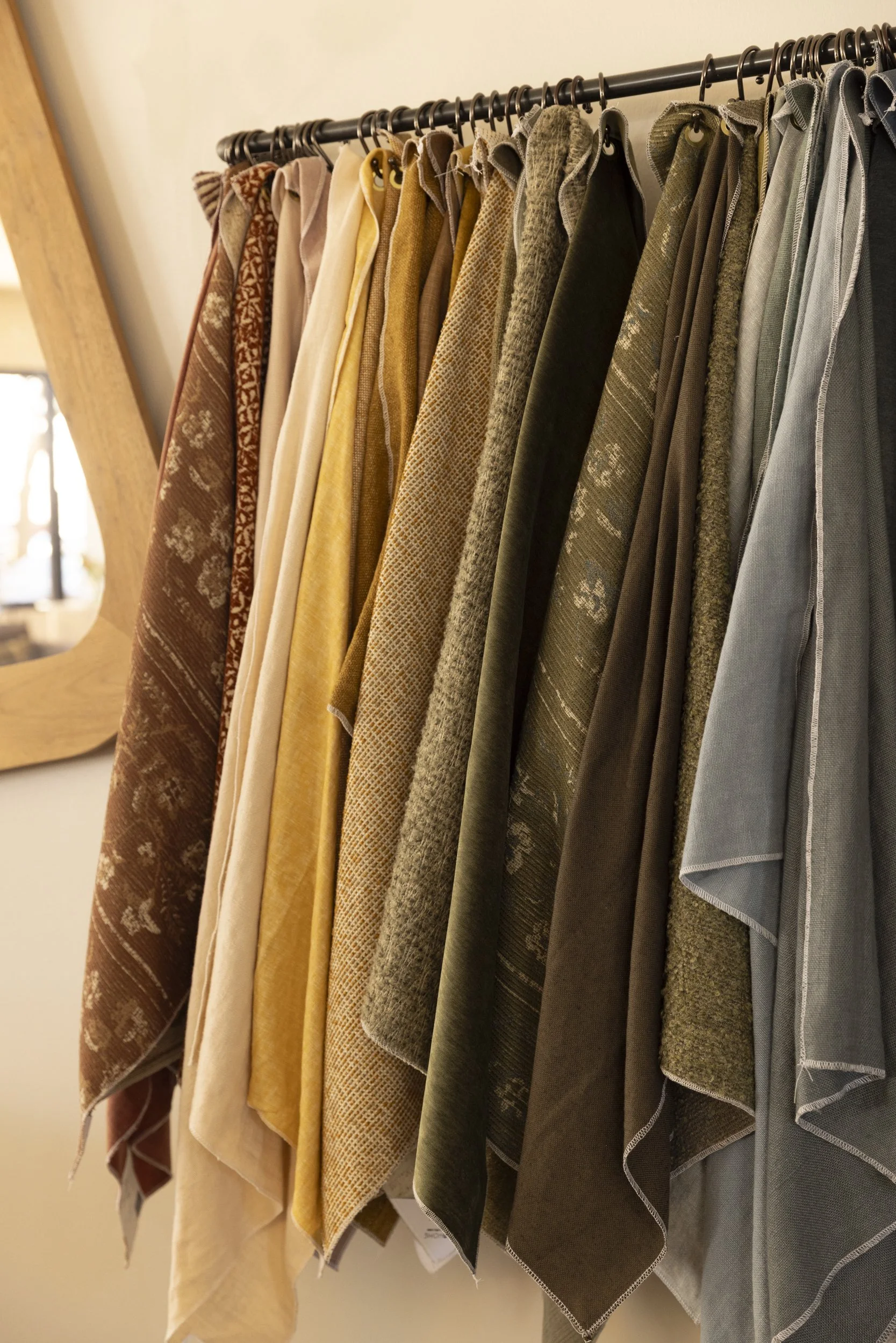 A display rack of various fabric napkins or hand towels in shades of brown, yellow, green, and gray hanging from hooks.