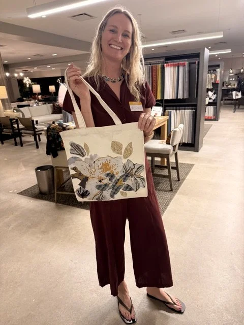 A woman smiling and holding a floral tote bag in a store or showroom.