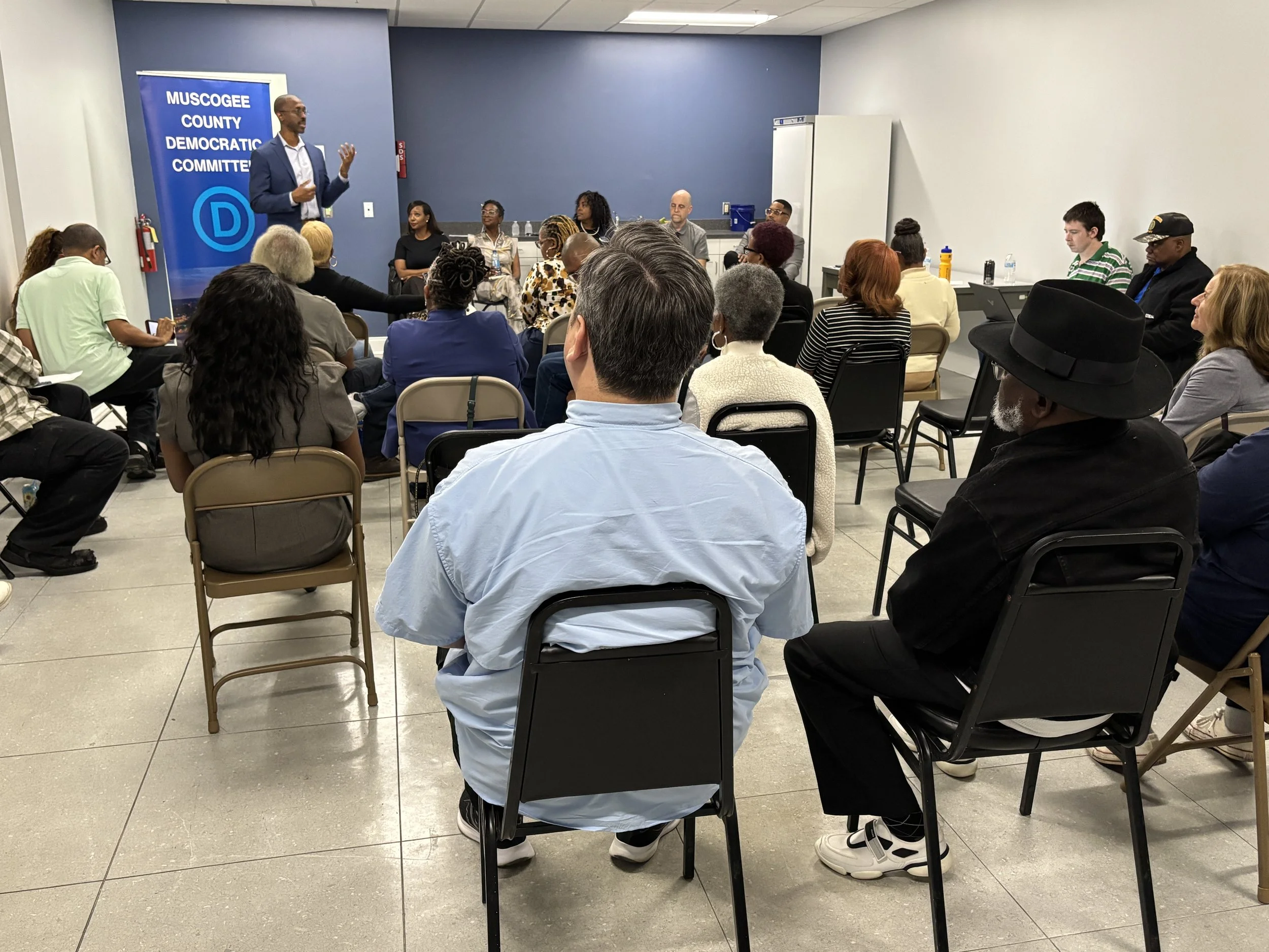 Black man in a navy suit speaks in front of a packed room