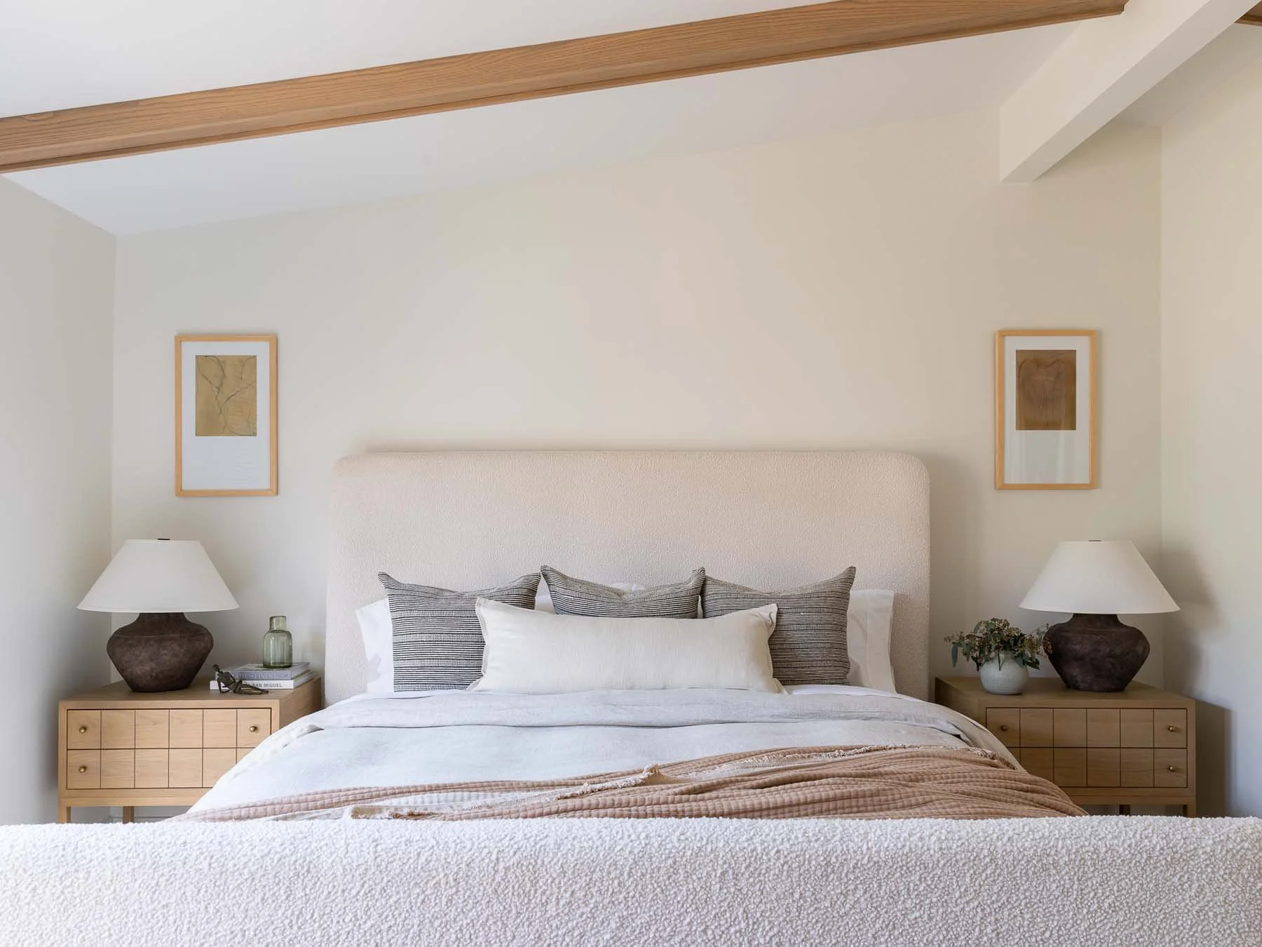 A cozy bedroom with a bed, striped pillows, nightstands with lamps, framed artwork, and decorative plants.