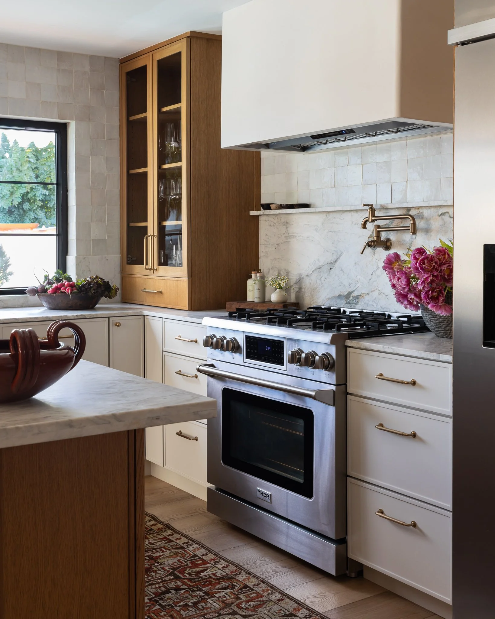 Modern kitchen with white and wood cabinetry, stainless steel oven, marble countertops, and flowers on the counter.