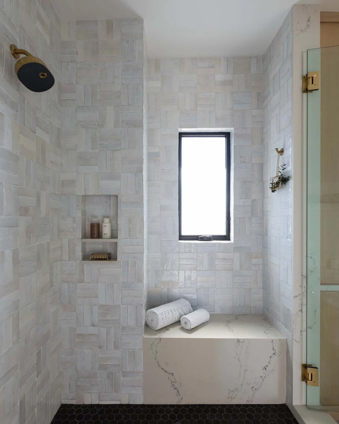 Modern bathroom with white textured tile walls, black hexagonal floor tiles, a small window, and a marble ledge with rolled white towels.