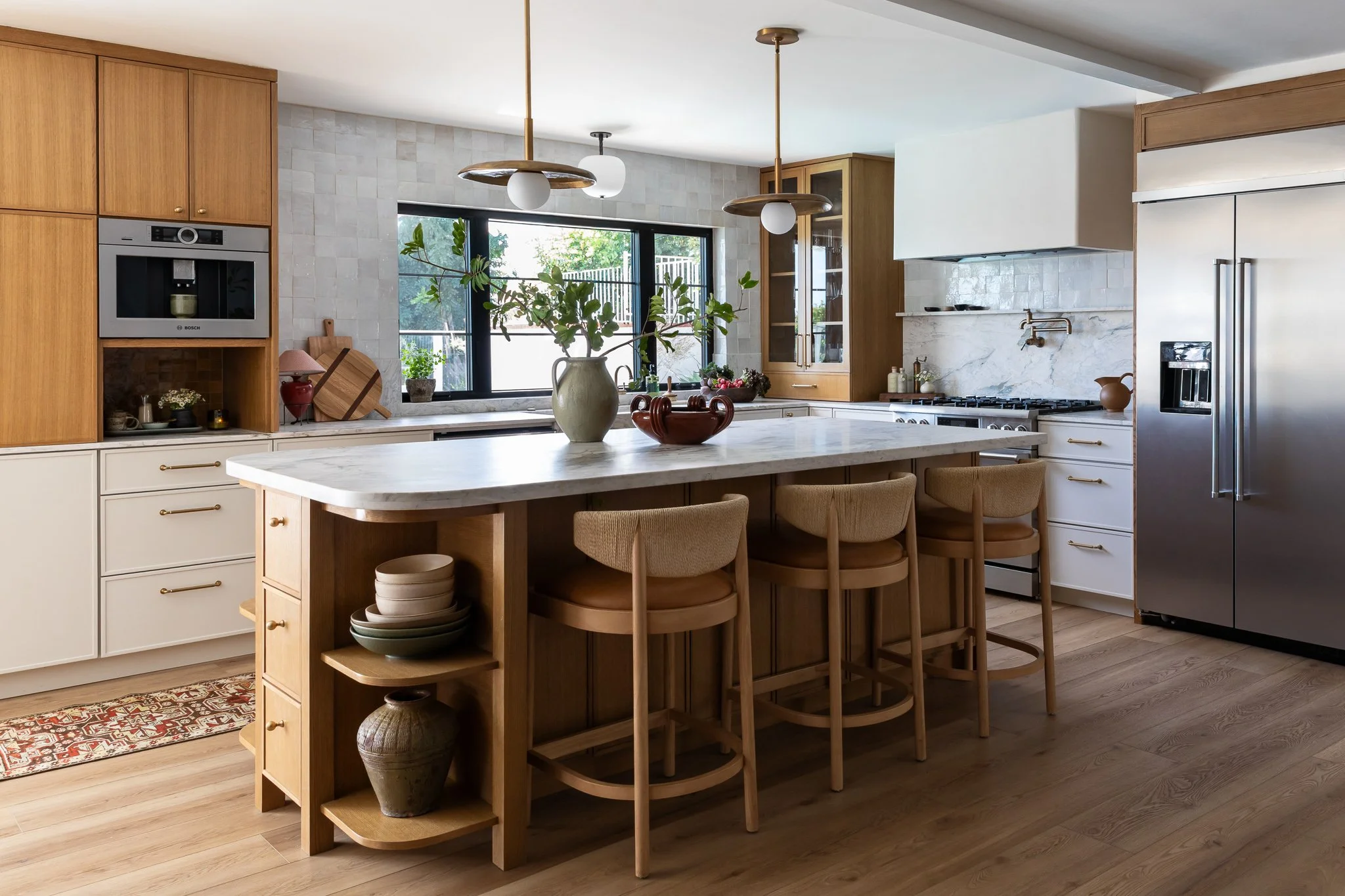 Kitchen with wooden cabinets, marble island, pendant lights, large window, and stainless steel refrigerator.