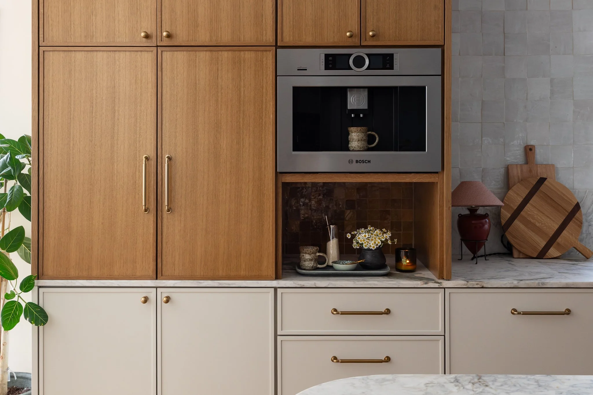 Kitchen cabinets with a built-in Bosch coffee machine, shelves with cups, bowls, a vase with flowers, a candle, and decorative items against a tiled wall.