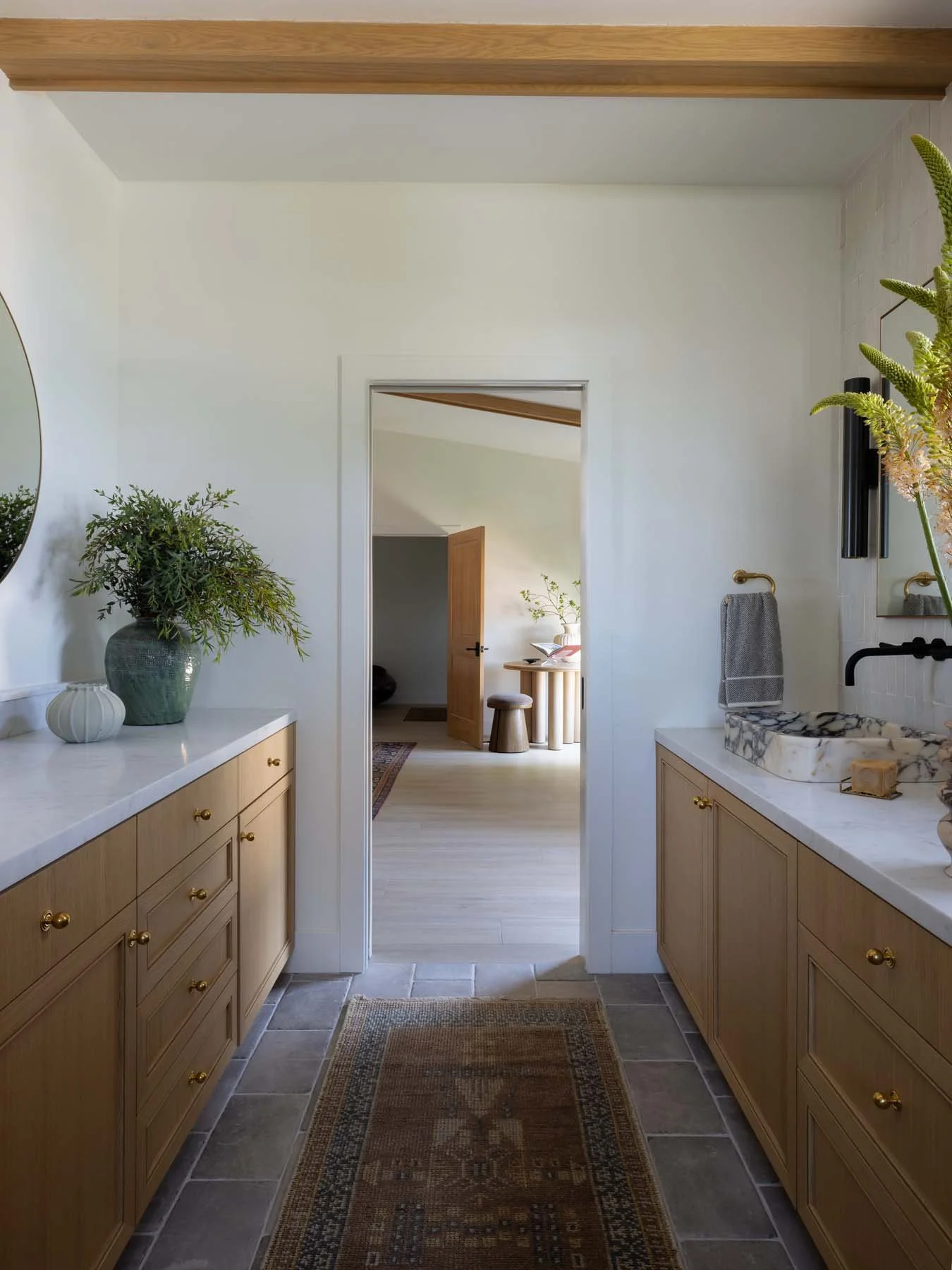 View through a doorway into a hallway with sitting area, plant, mirror, and natural wood accents.