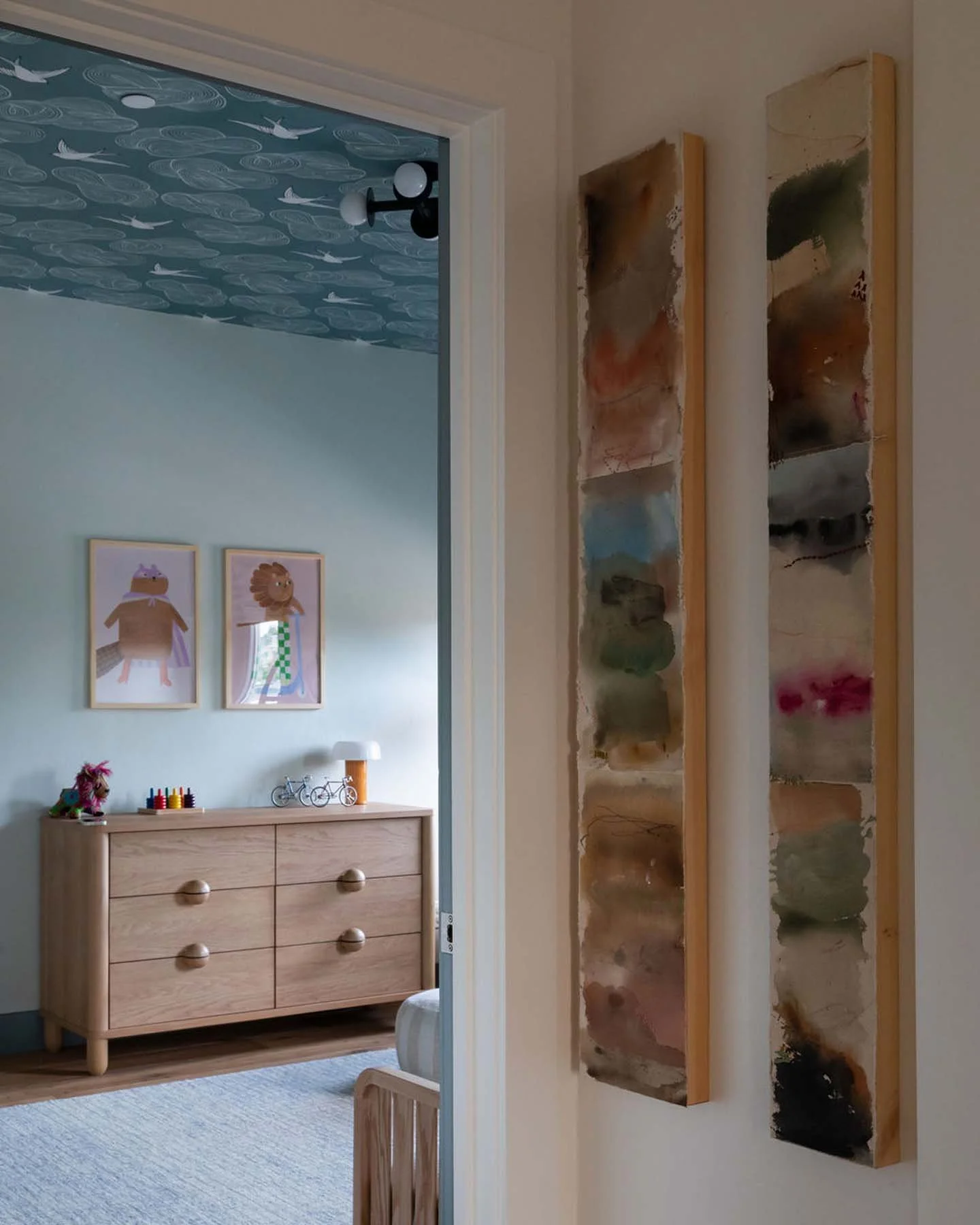 Interior view of a room with a watercolor art piece on the wall, a wooden dresser with toys and decorative items, and a ceiling with ocean-themed wallpaper featuring whales.