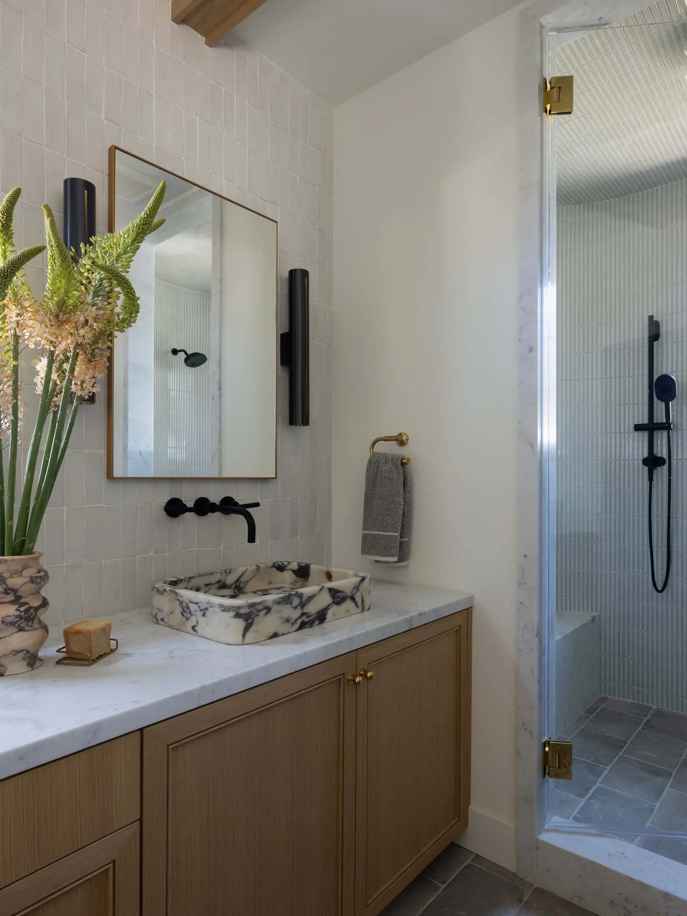 Bathroom with a marble sink, wooden cabinet, mirror, and a glass shower stall.