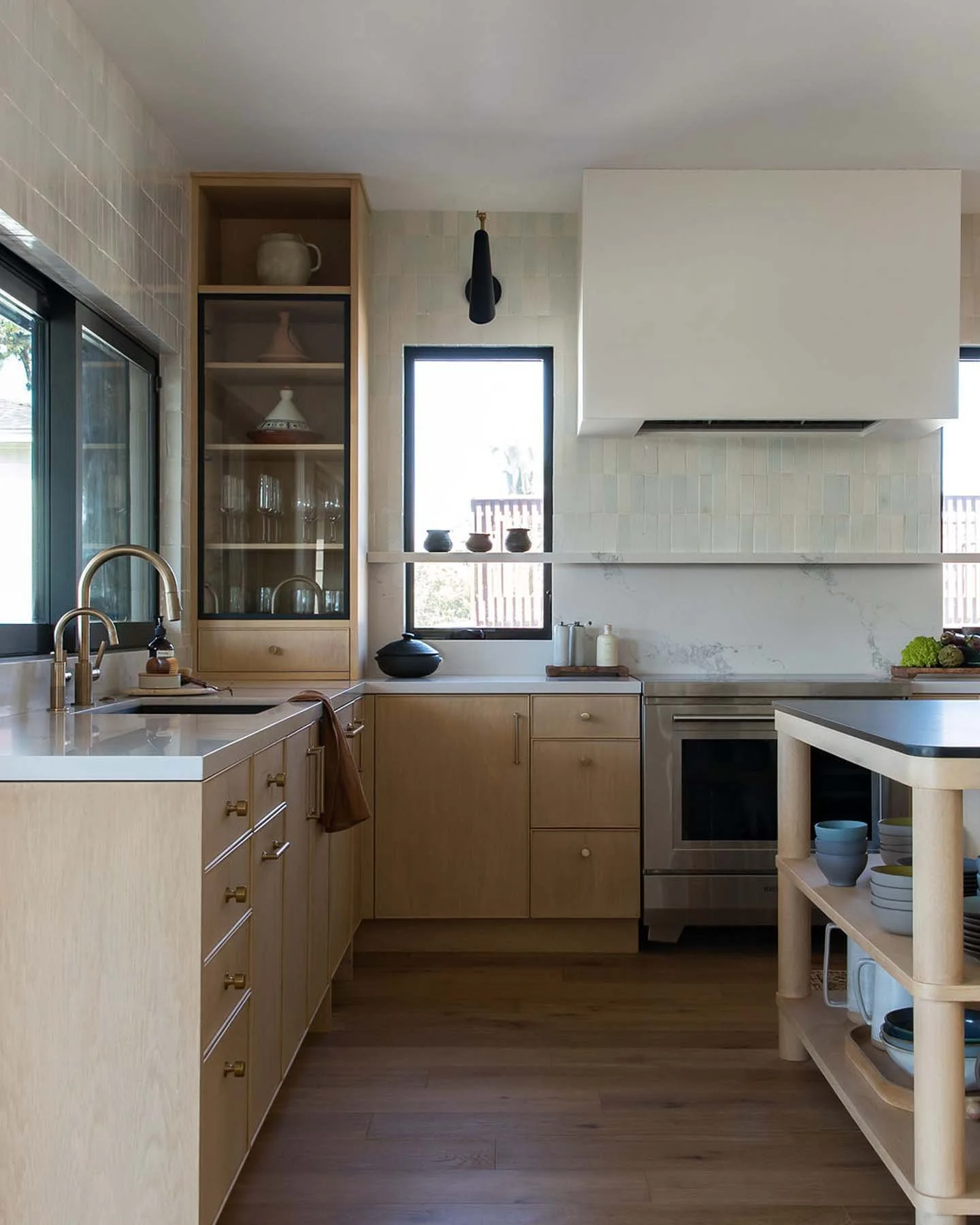 Modern kitchen with light wood cabinets, a black window, a stove, and a small rolling cart with stacked bowls.