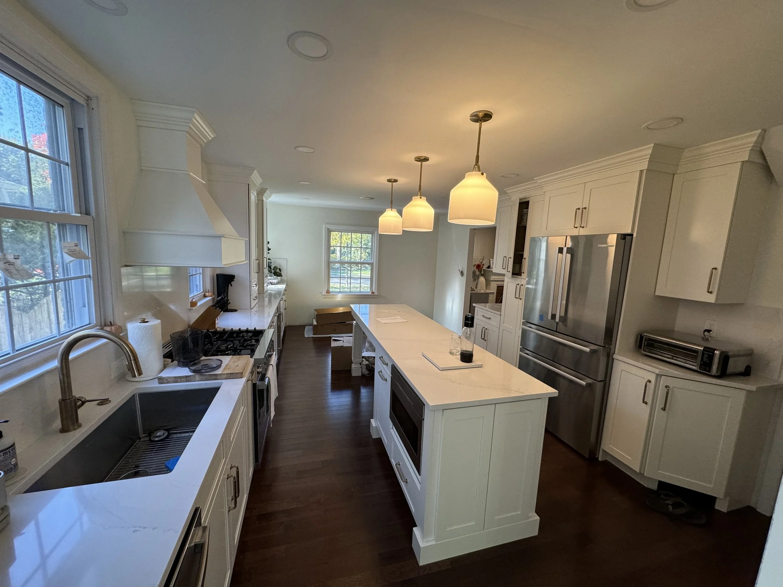A modern kitchen with white cabinets, a kitchen island, stainless steel appliances, and three pendant lights hanging from the ceiling.