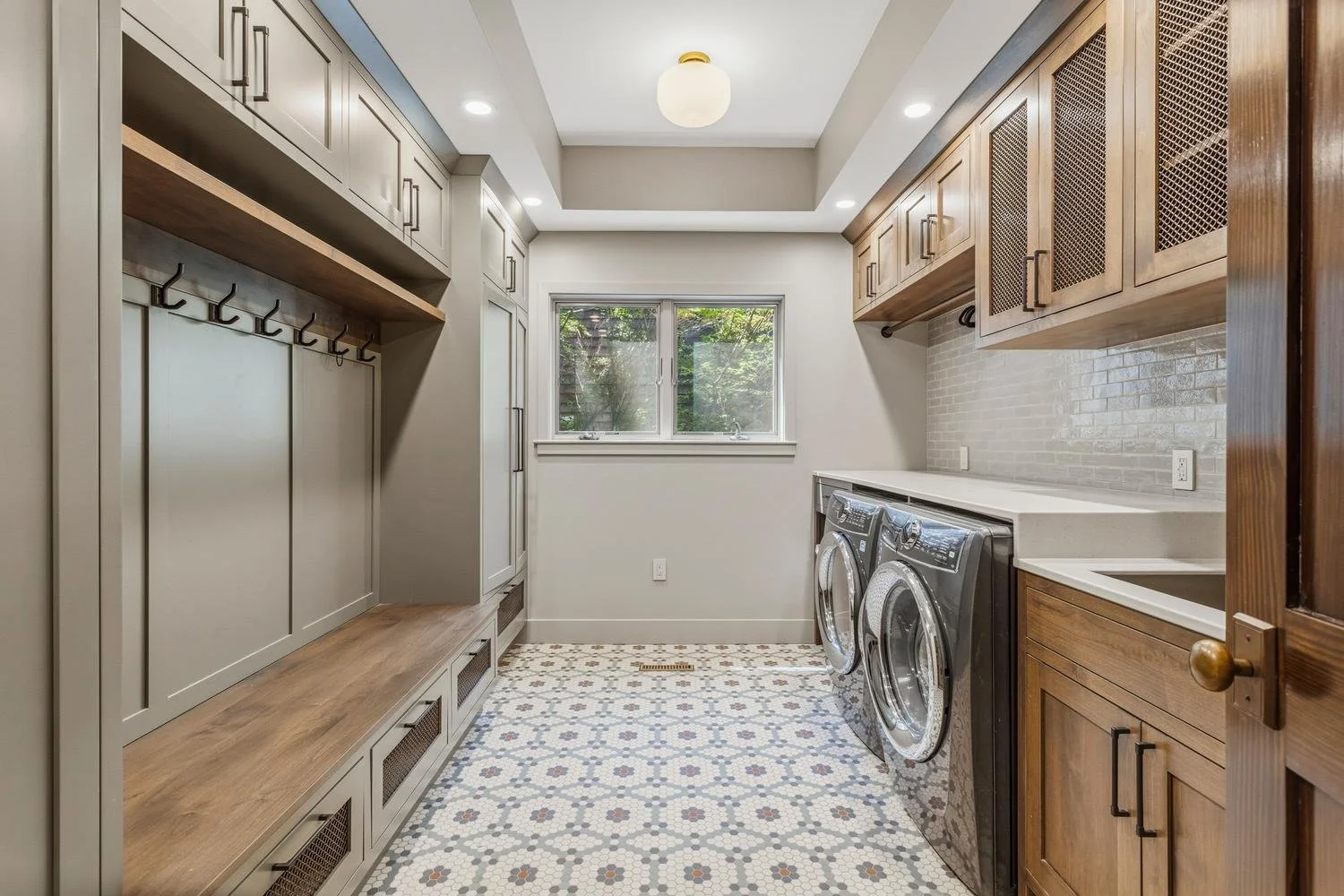 Trent Meacham luxury house listing in Champaign-Urbana of laundry room with a window, washer and dryer, wooden cabinets, hooks, and a tiled floor.