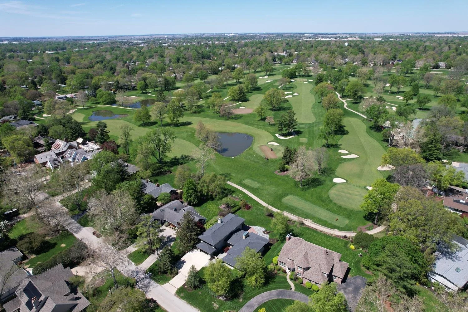 Trent Meacham Real Estate aerial view of a Champaign Country Club golf course home for sale with several holes, water hazards, and trees, surrounded by residential houses and roads.