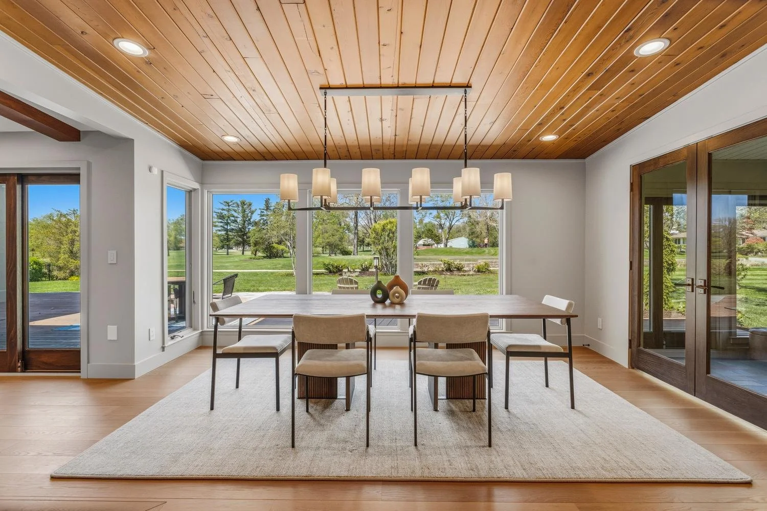 Realtor Trent Meacham's luxury house listing of a modern dining room with a large window overlooking the Champaign Country Club golf course. Glass doors on either side of the window lead to an outdoor space.
