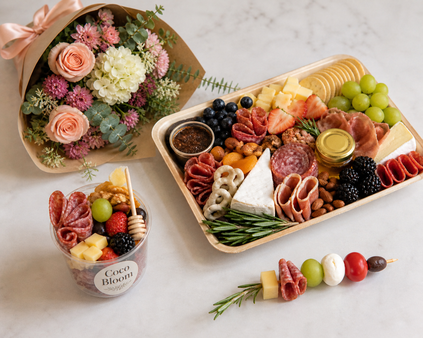 A charcuterie board with cheese, meats, grapes, blackberries, strawberries, nuts, and honey, alongside a flower bouquet and a smaller cup of mixed fruits and cheese.