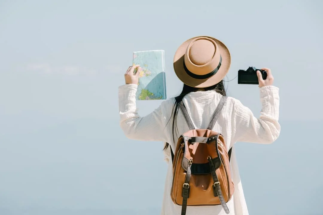 young woman traveler standing wearing a backpack, holding a map and camera