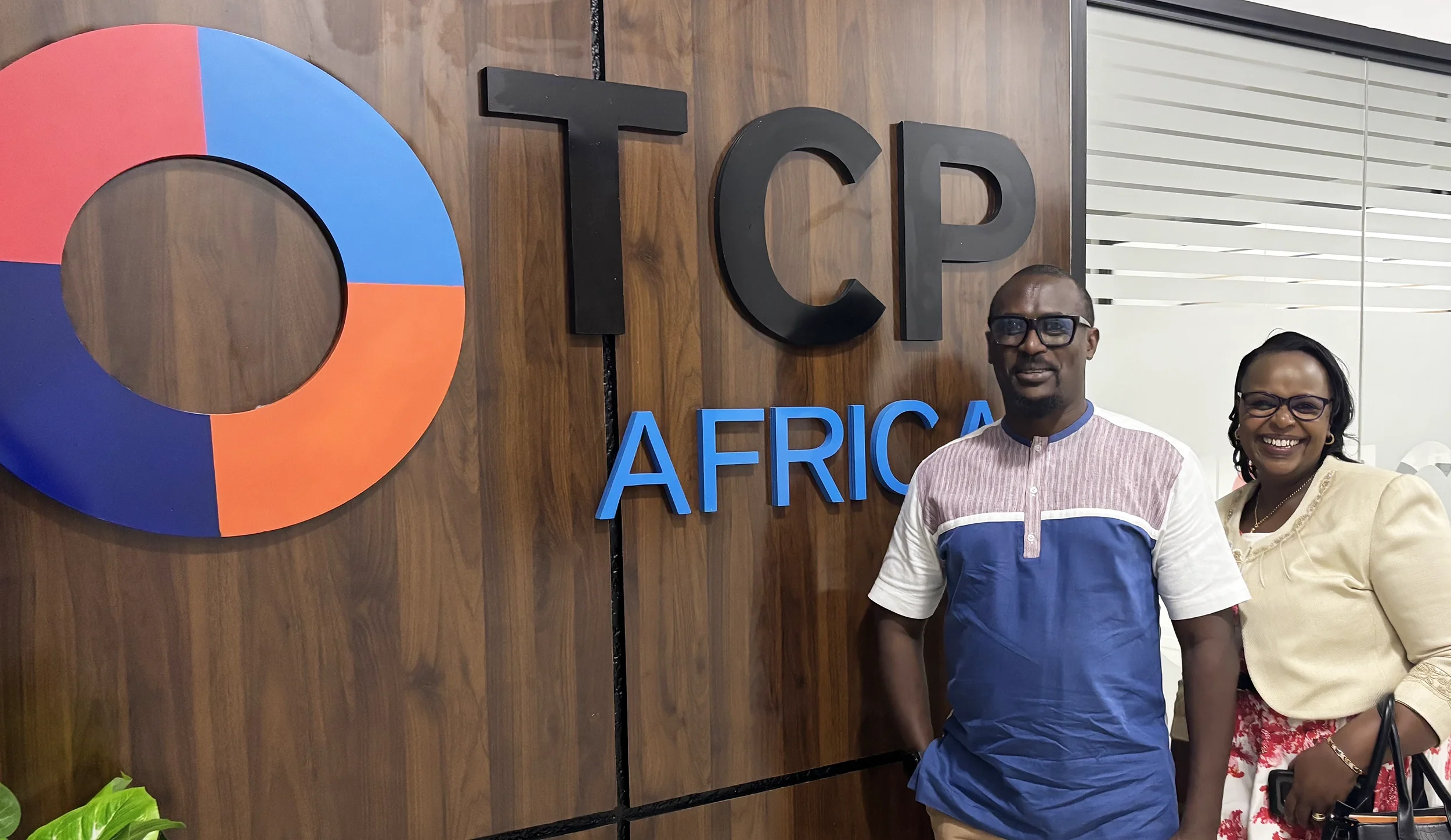 An African man and woman standing in the TCP Africa office in front of a sign that says TCP Africa