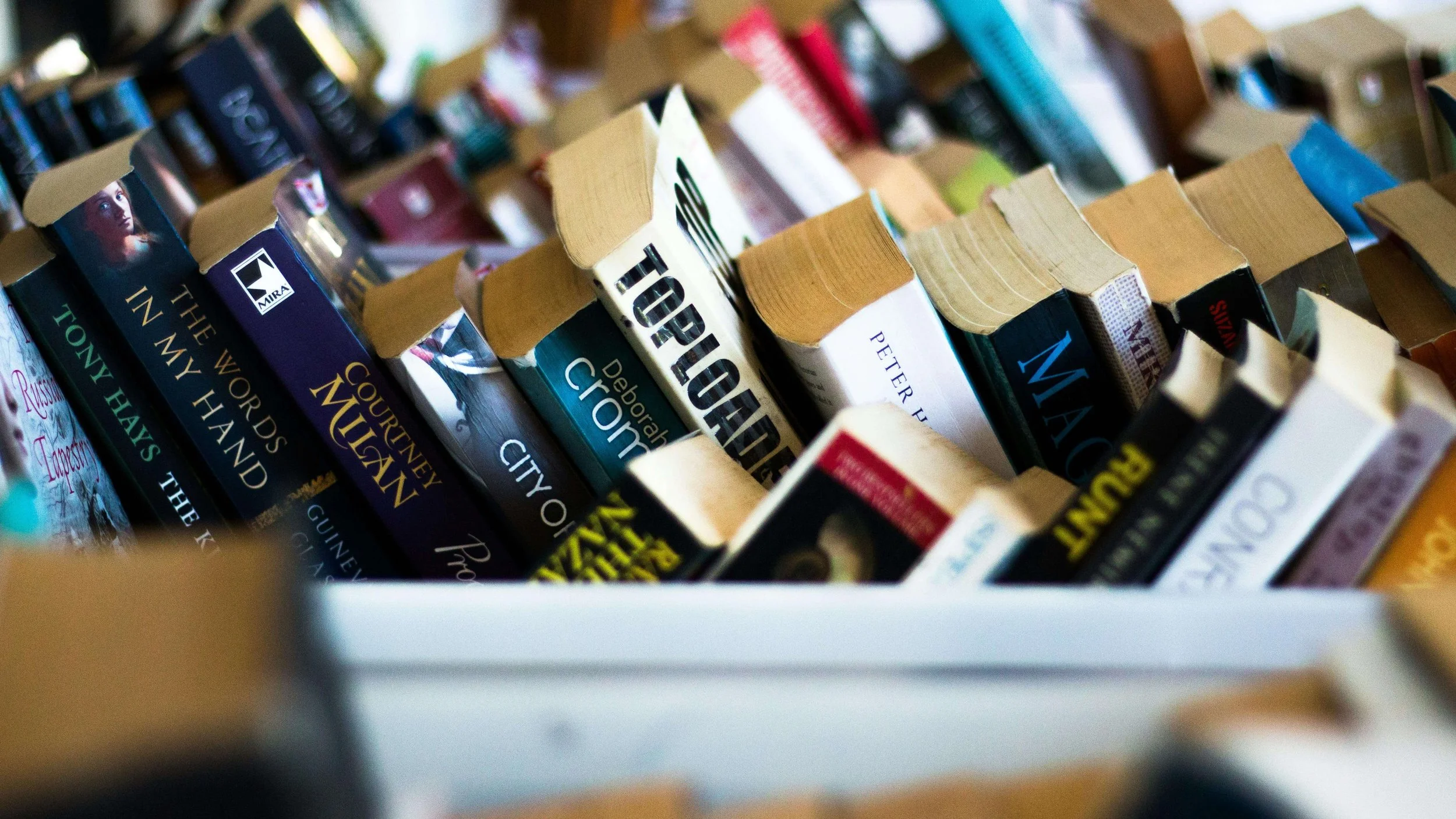 A box of used paperback books available for swapping at a community book swap event at Paper Boat Booksellers in the West Seattle Junction