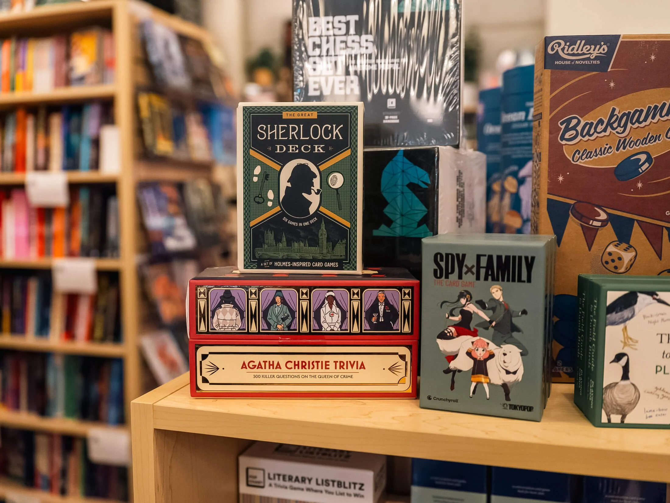 Games and gifts display at Paper Boat Booksellers in West Seattle, featuring Agatha Christie Trivia, The Great Sherlock Deck, Spy x Family card game, and classic wooden backgammon