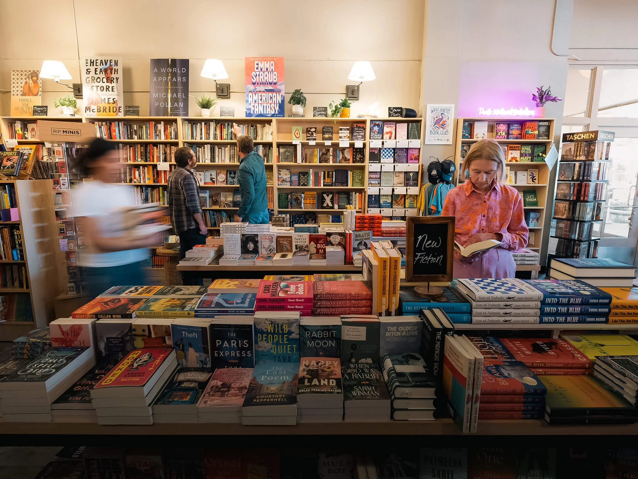 Interior of Paper Boat Booksellers in West Seattle with customers browsing a large new fiction table display and shelves of books