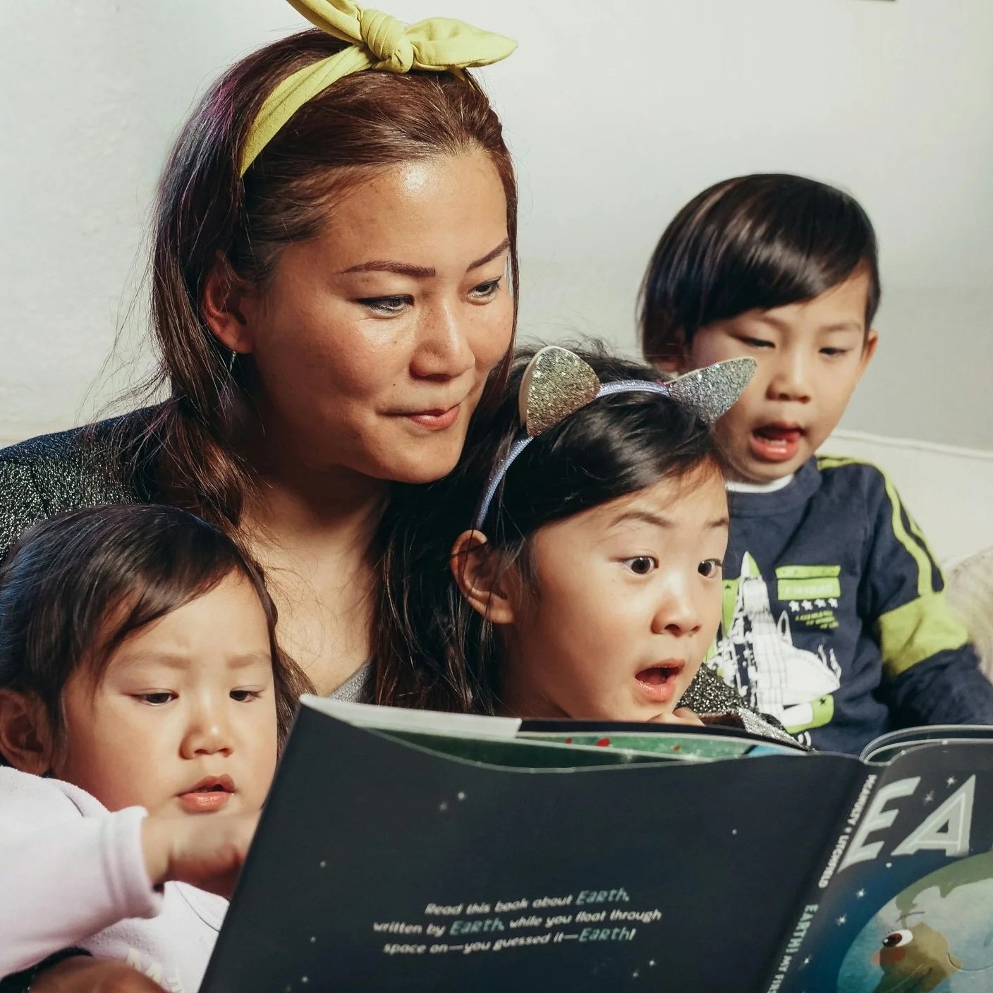 A parent reading a picture book to three young children during Family Reading Time at Paper Boat Booksellers in West Seattle, a free weekly event held Saturday mornings at the independent bookstore