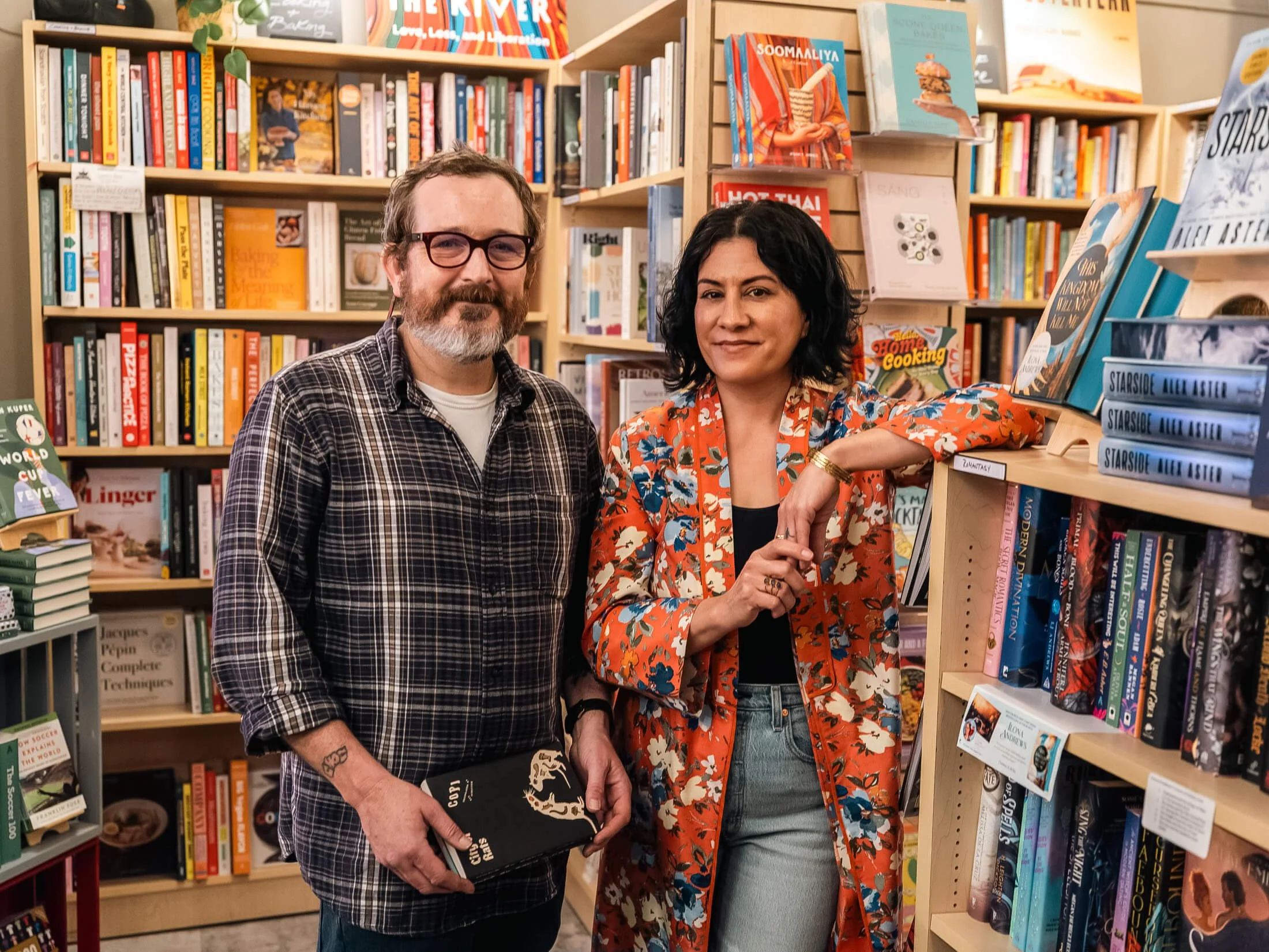 Paper Boat Booksellers founders Desirae and Eric standing together among the bookshelves of their West Seattle independent bookstore