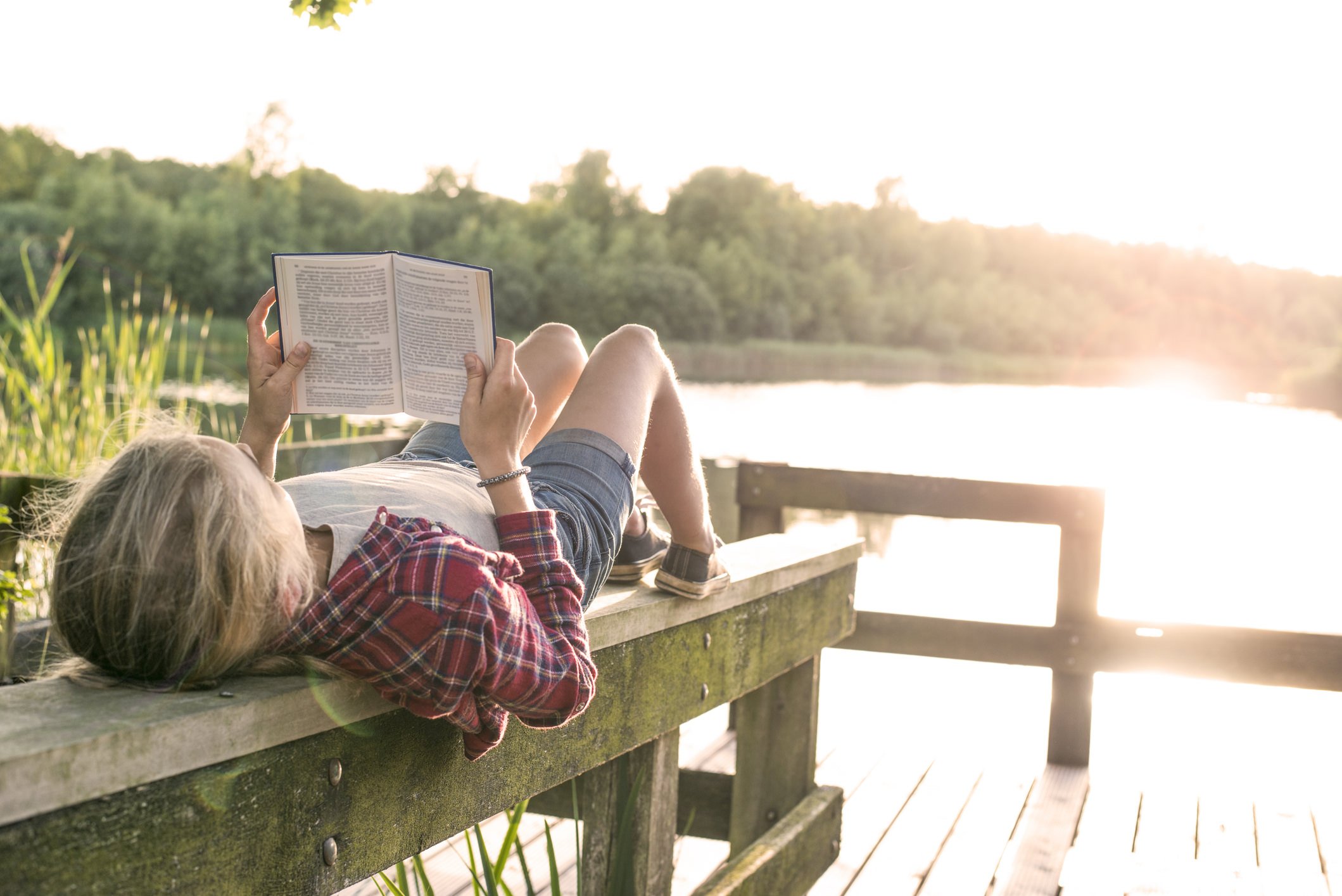 Person lying on a dock reading a book on a sunny summer evening