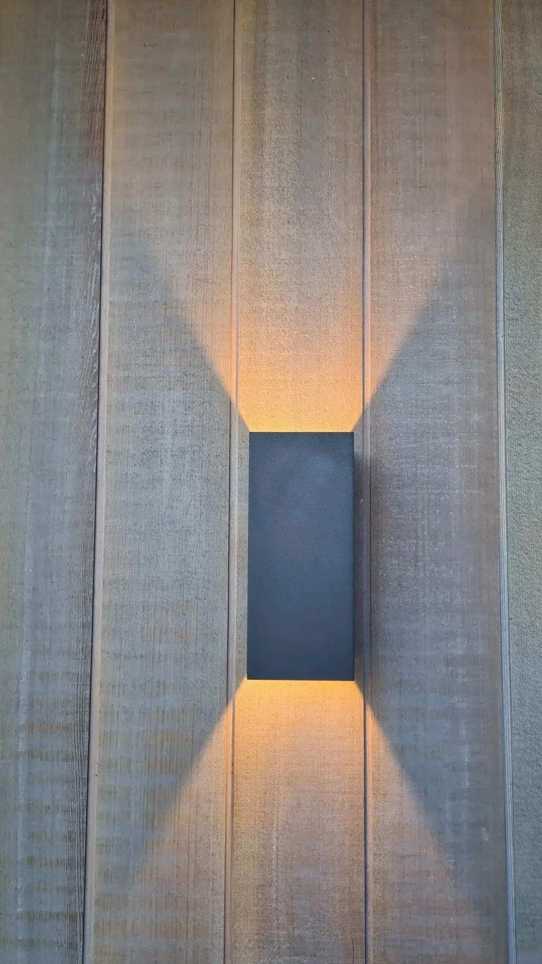 Wall sconce light fixture casting a vertical V-shaped shadow on a wooden wall.