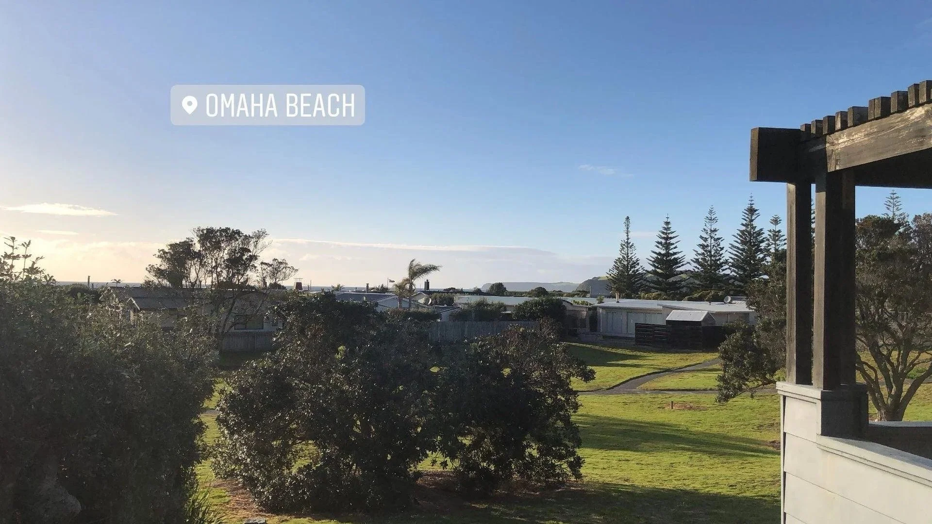 View of Omaha Beach with houses, trees, and a clear sky, seen from a balcony or porch.