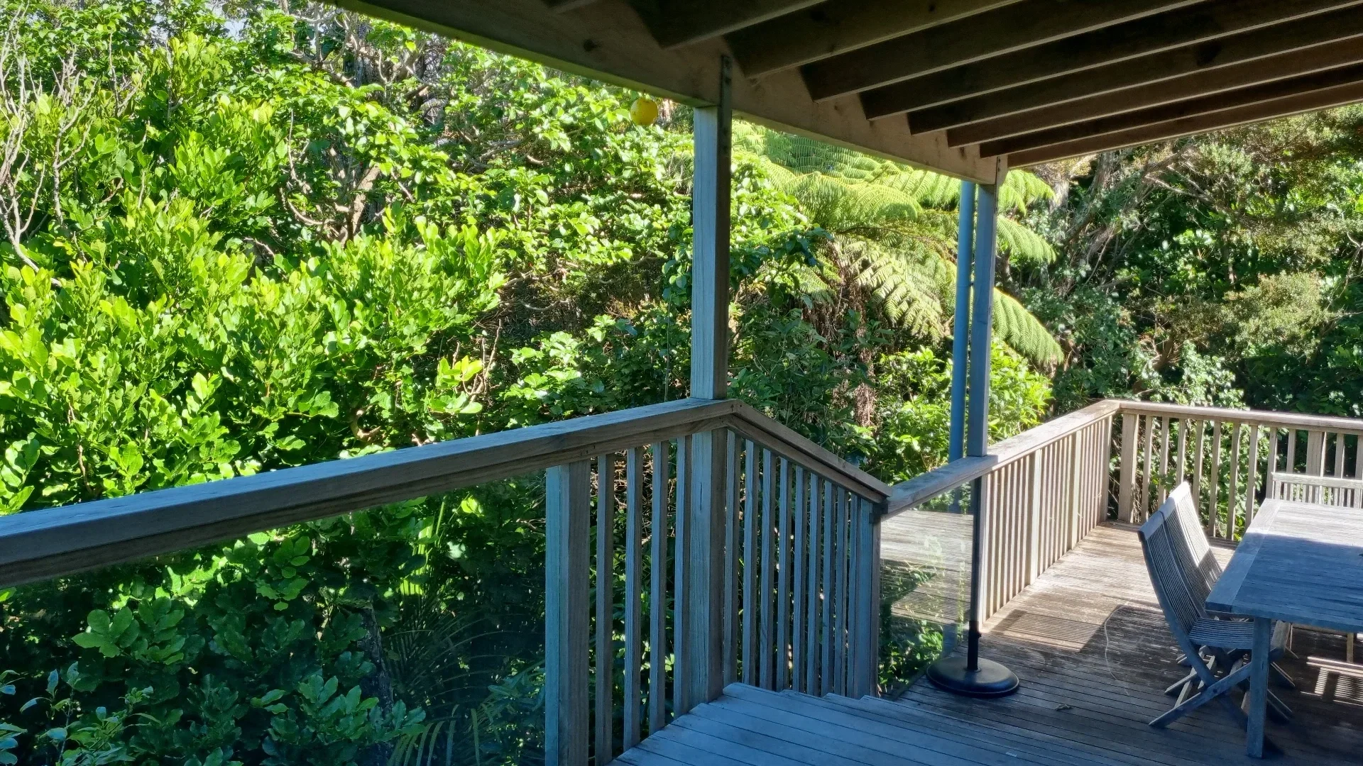 A wooden balcony with an outdoor table and chairs overlooking lush green trees and foliage.