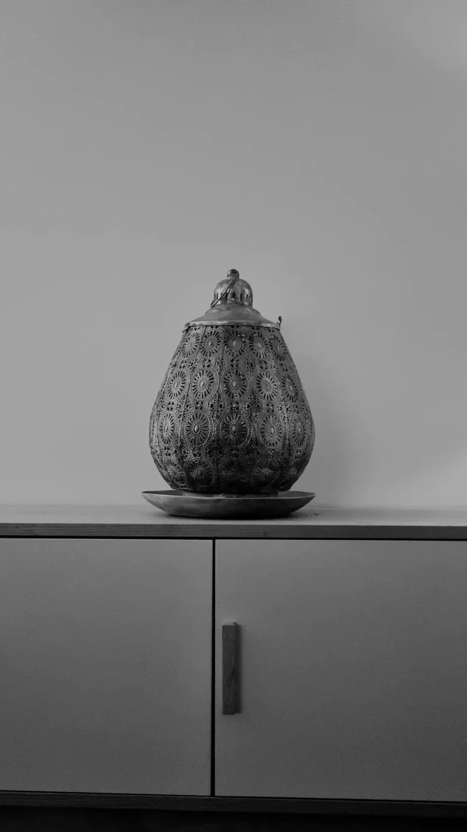 A decorative metal lantern with intricate circular patterns, placed on a round tray on top of a cabinet.