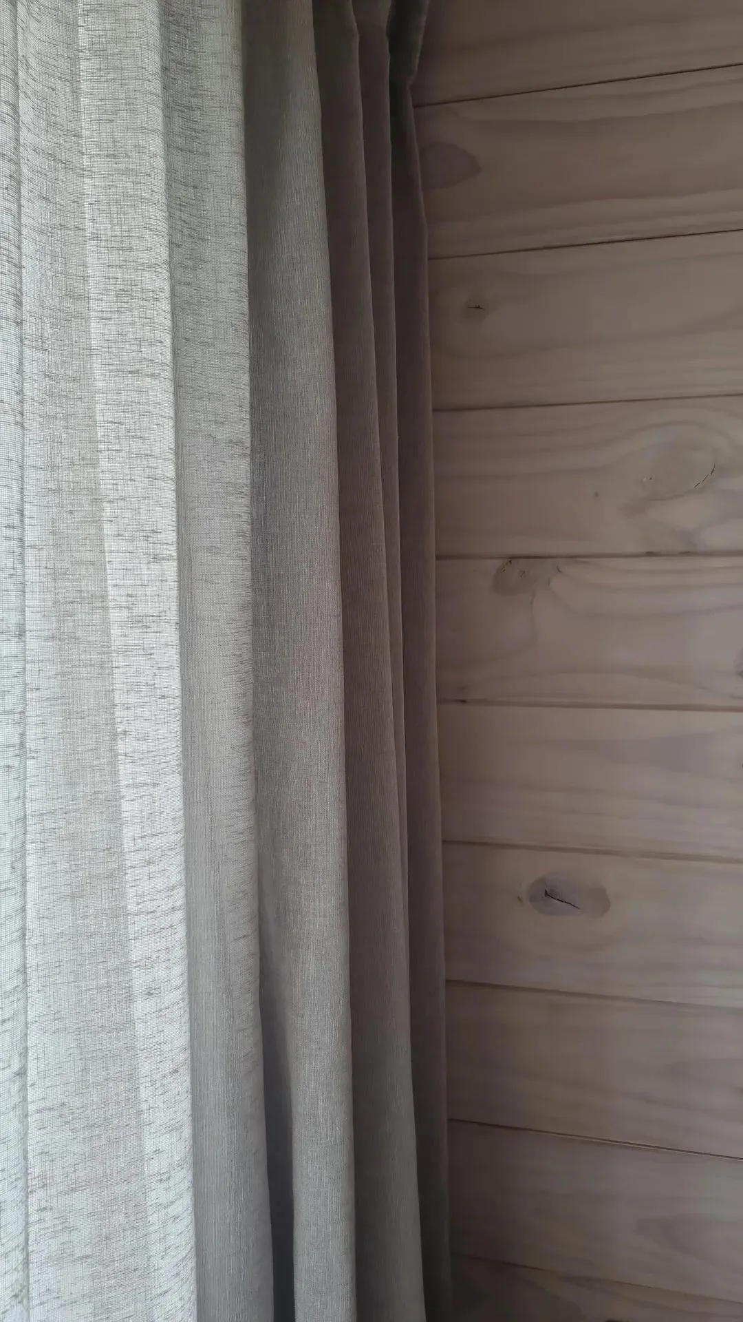 Close-up of beige curtains overlapping on a wooden wall.