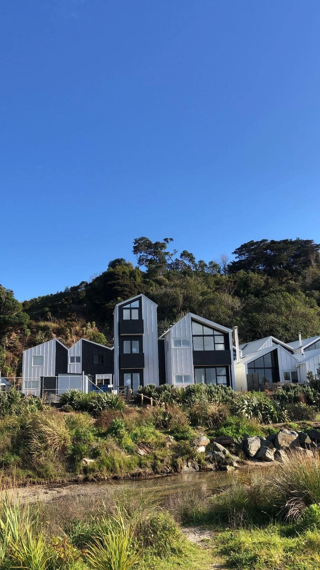 Modern white and black houses on a hillside with a clear blue sky and greenery around.