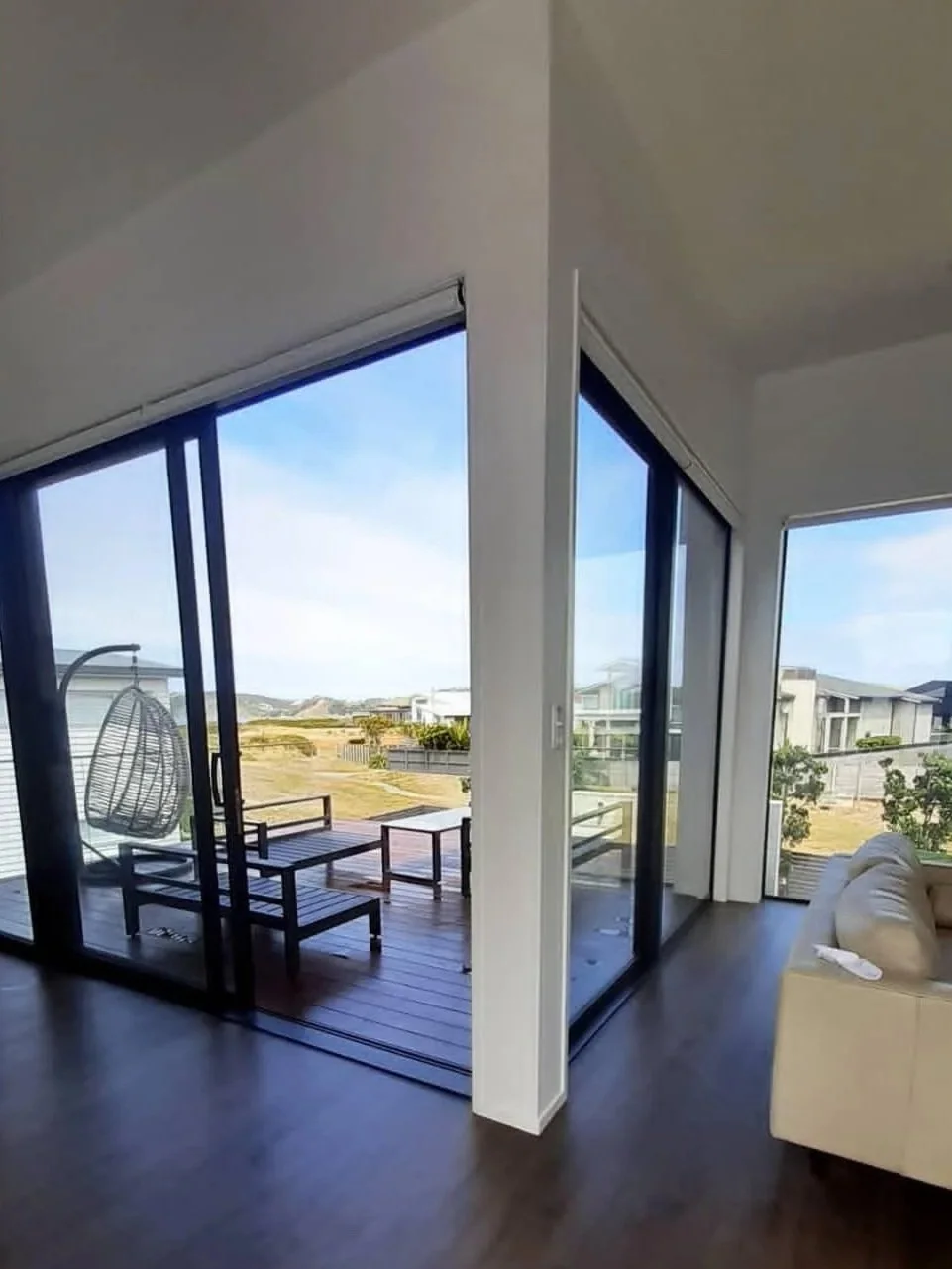 Living room with glass sliding doors leading to a balcony, outdoor furniture, and a view of neighboring houses and a grassy landscape.