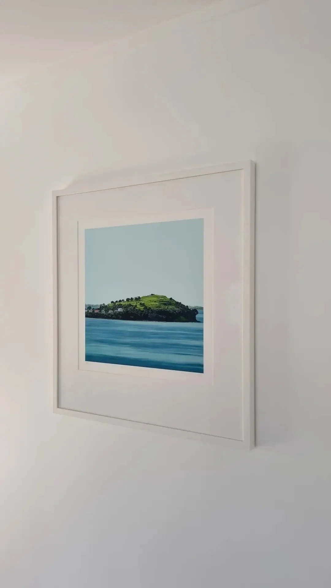 Framed photograph of a coastal hill island viewed from the shore, with blue ocean in the foreground and a clear sky.
