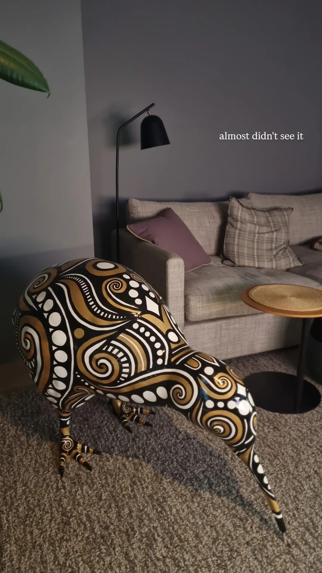 A living room with a patterned chair resembling an animal, beige sofa with pillows, black floor lamp, and a small round wooden table, with the text 'almost didn't see it' on the wall.