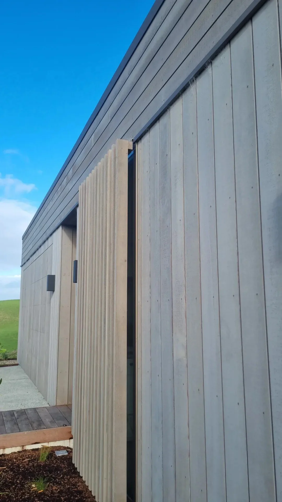 Modern building with vertical wooden siding, metal accents, and a landscaped foreground against a blue sky.
