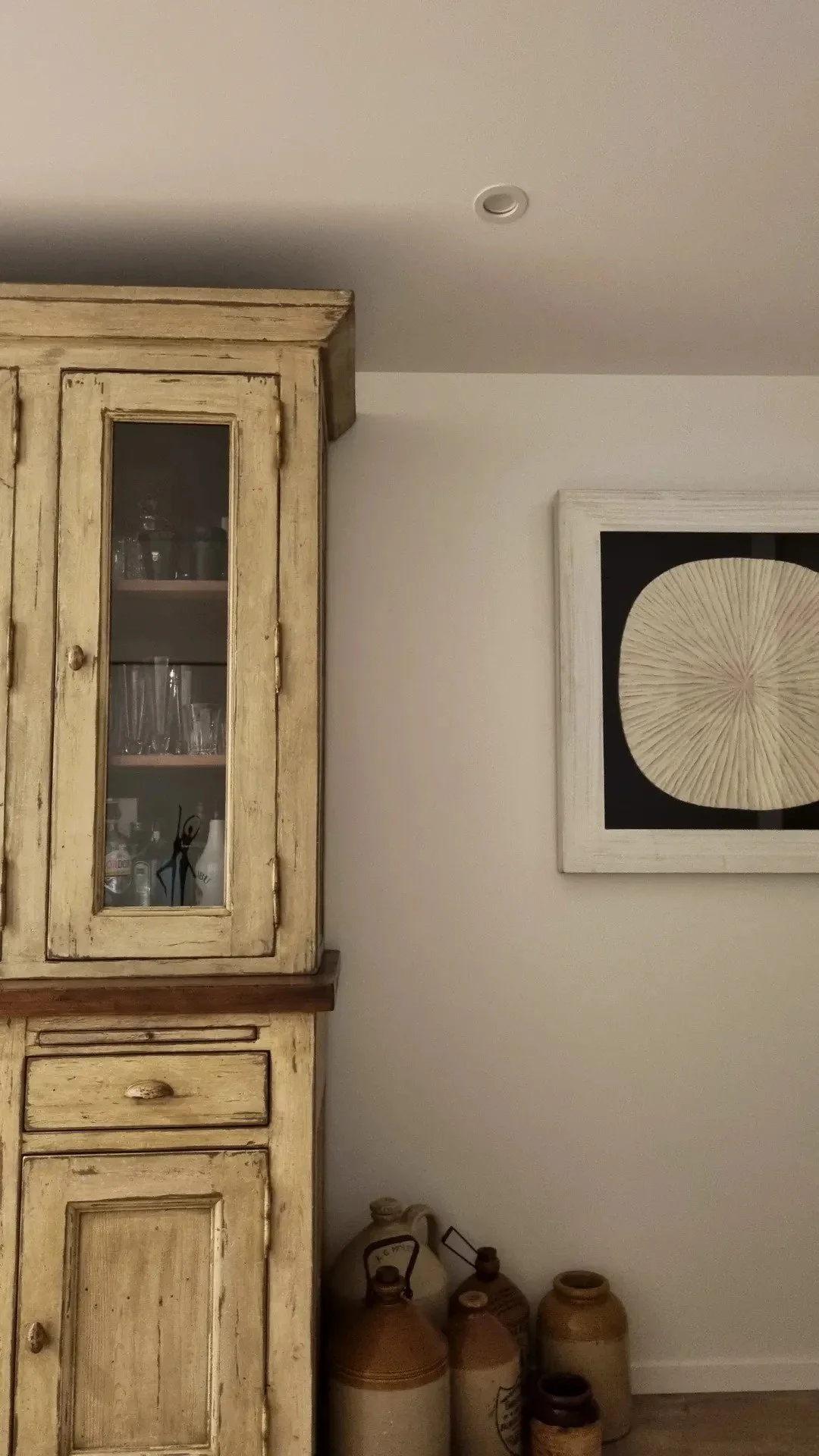 Part of a living room with a rustic wooden cabinet, framed wall art, and a collection of clay pots on the floor.