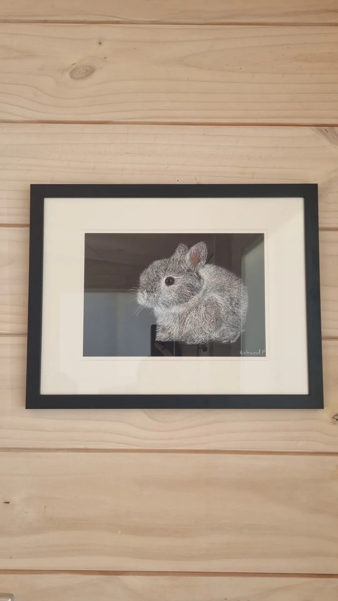 Framed black-and-white photograph of a small rabbit on a light wooden wall.