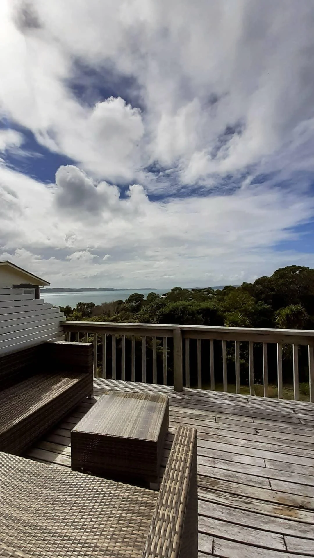 A wooden deck with outdoor furniture overlooking a landscape with trees, water, and a cloudy sky.