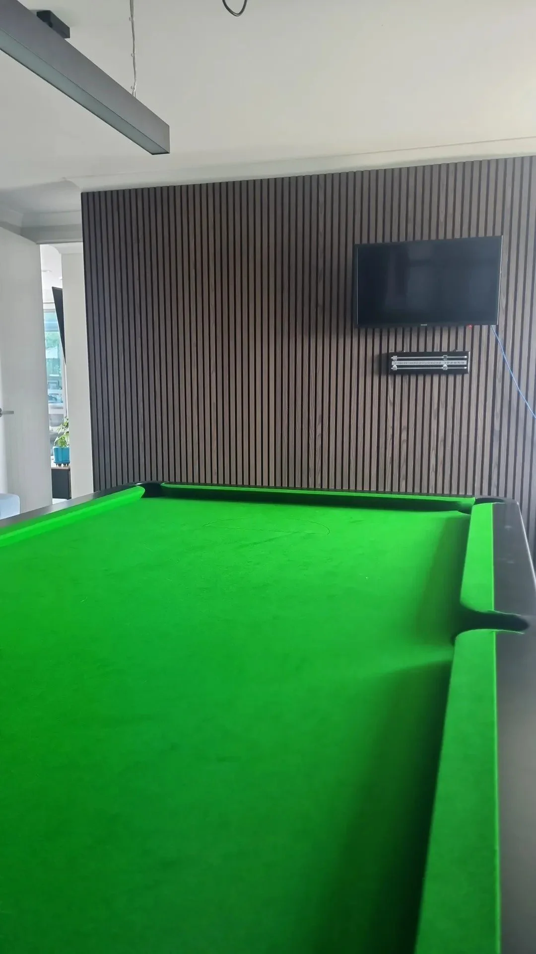 Indoor billiards room with green pool table, dark wood paneled wall, television, and electronic scoreboard.