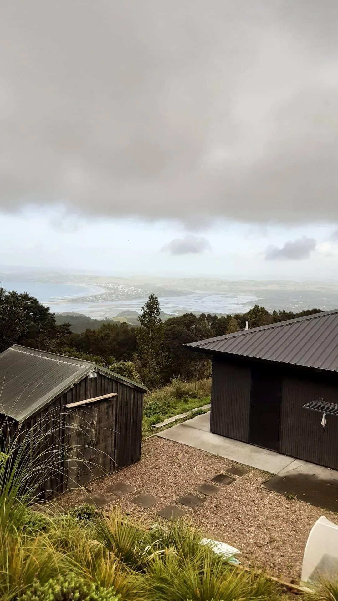 Overcast sky over a landscape with water, trees, and two wooden structures in the foreground.